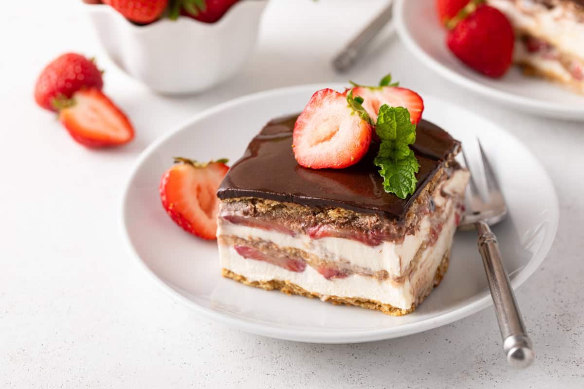 Slice of strawberry eclair cake garnished with fresh strawberries on a white plate.