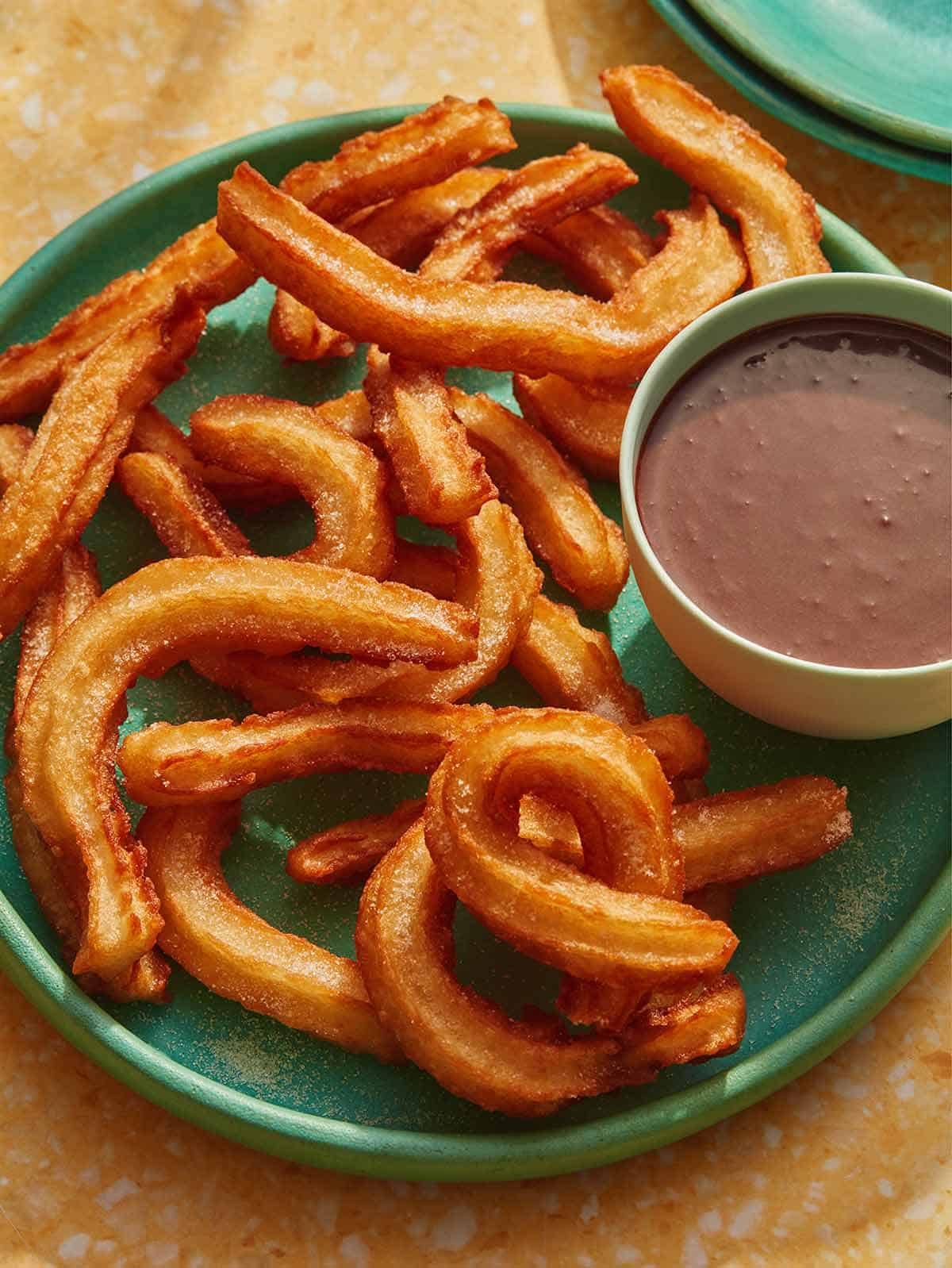 Spanish Churros on a plate with a bowl of chocolate sauce on the side.