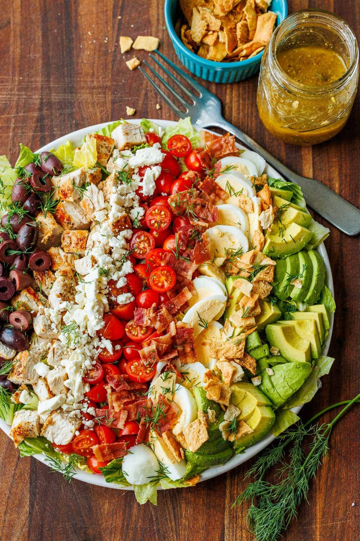 Large Greek Cobb Salad on a white plate with greek dressing in a mason jar