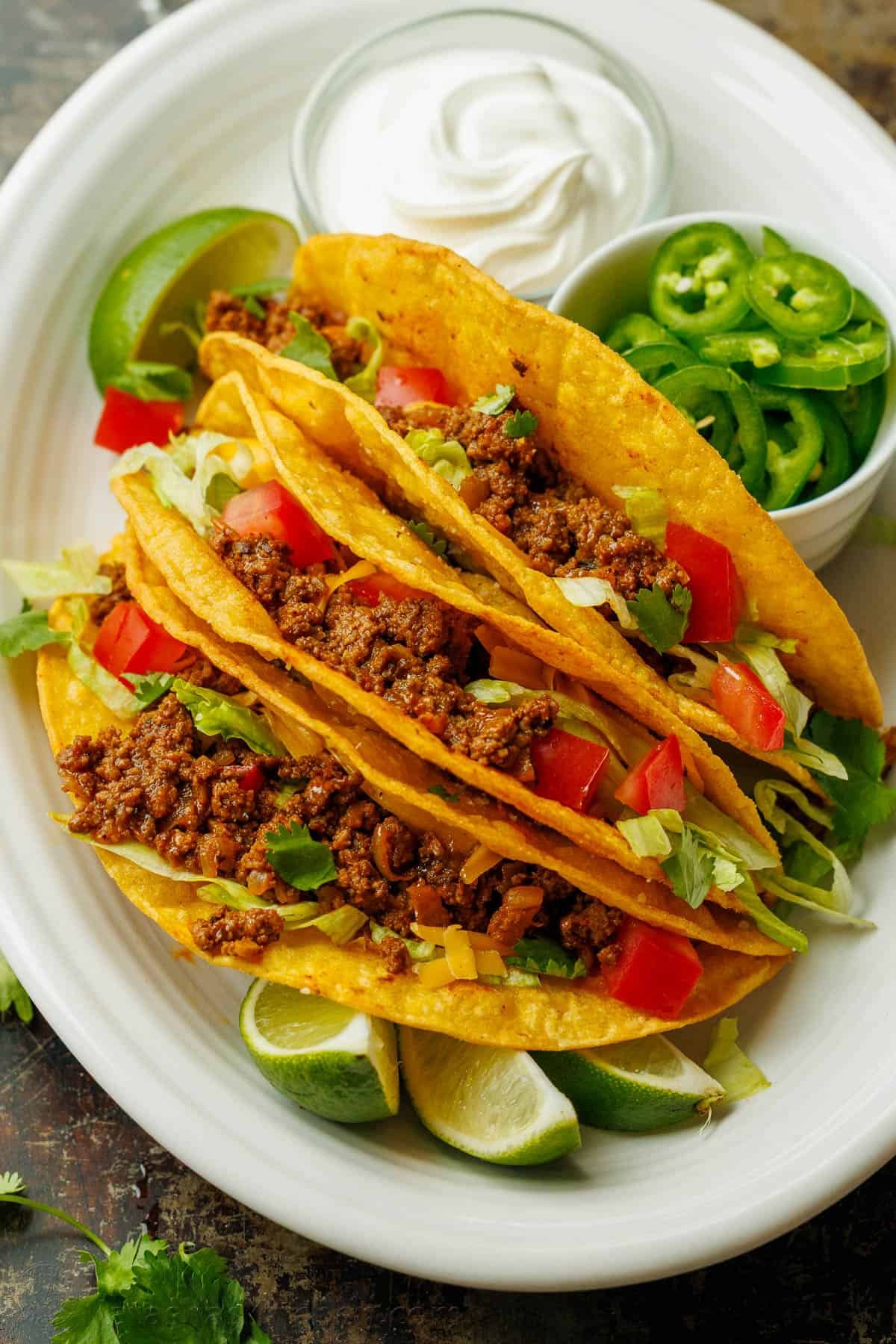 Ground beef nachos recipe on a white plate with sour cream, limes and sliced jalapeños.