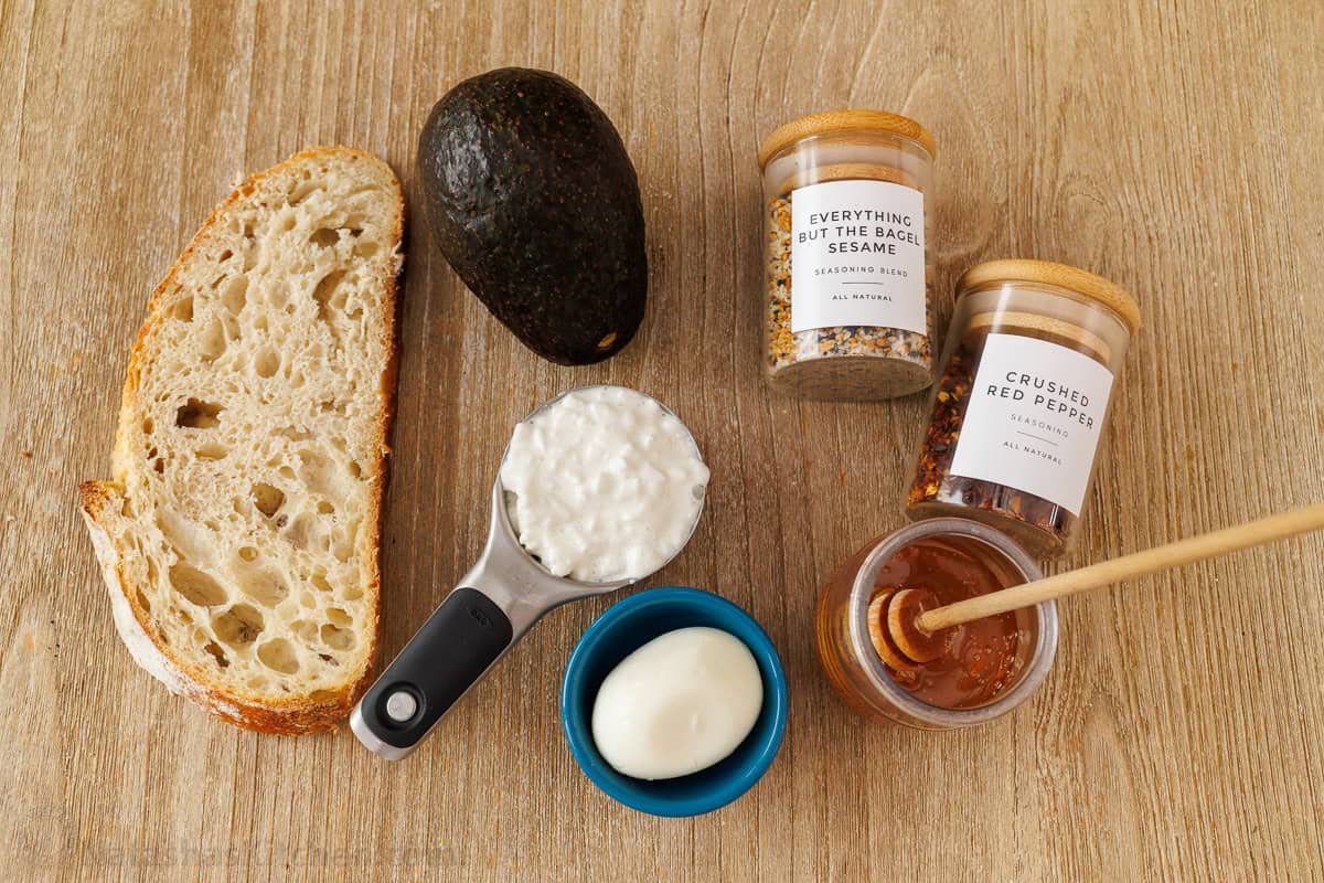 Ingredients for the best high-protein breakfast including bread, healthy fat, dairy, egg, everything but the bagel seasoning, crushed red pepper and honey