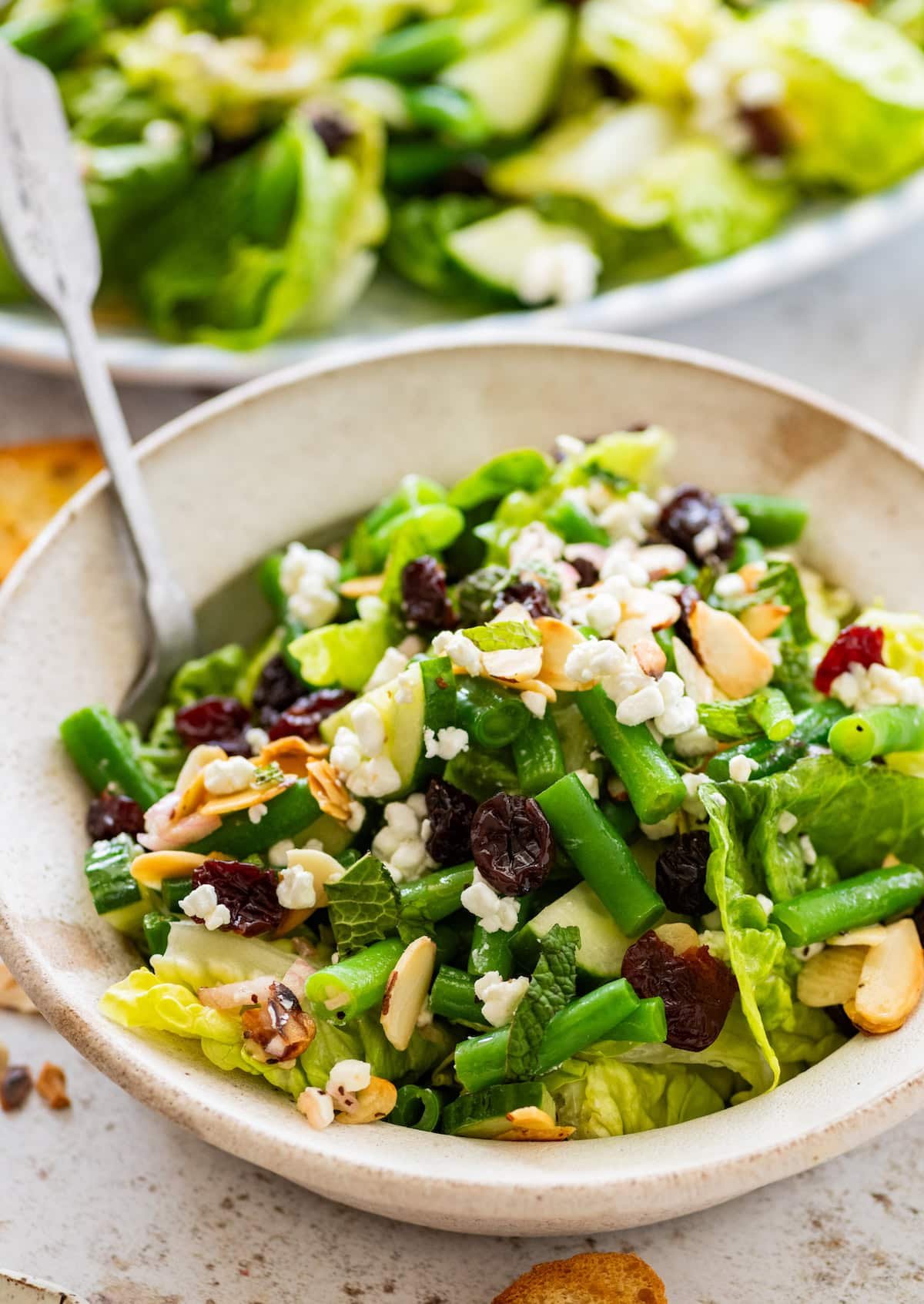 green bean salad with dried cherries, almonds, goat cheese, and mint in bowl with fork. 