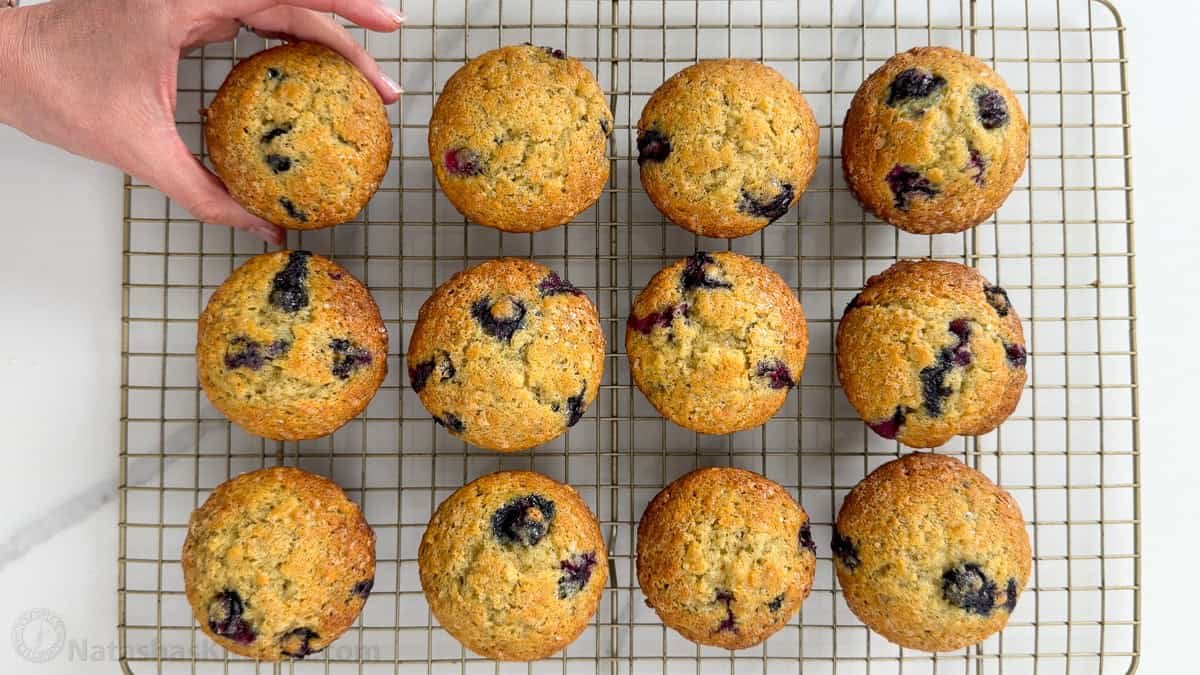 Hand removing a blueberry banana muffin from a cooling rack