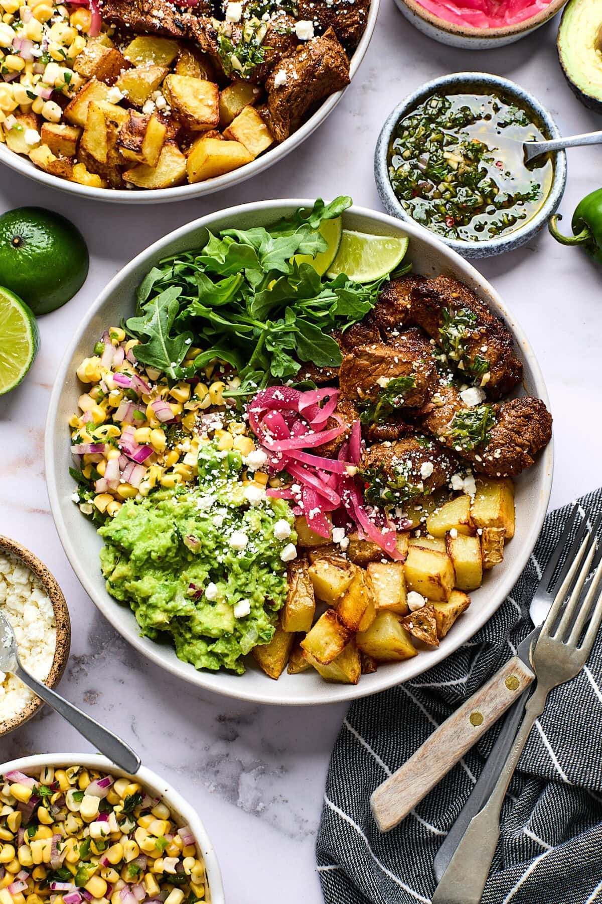 Steak Bowls with Roasted Potatoes, chimichurri, guacamole, corn salsa, arugula, and pickled red onions. 