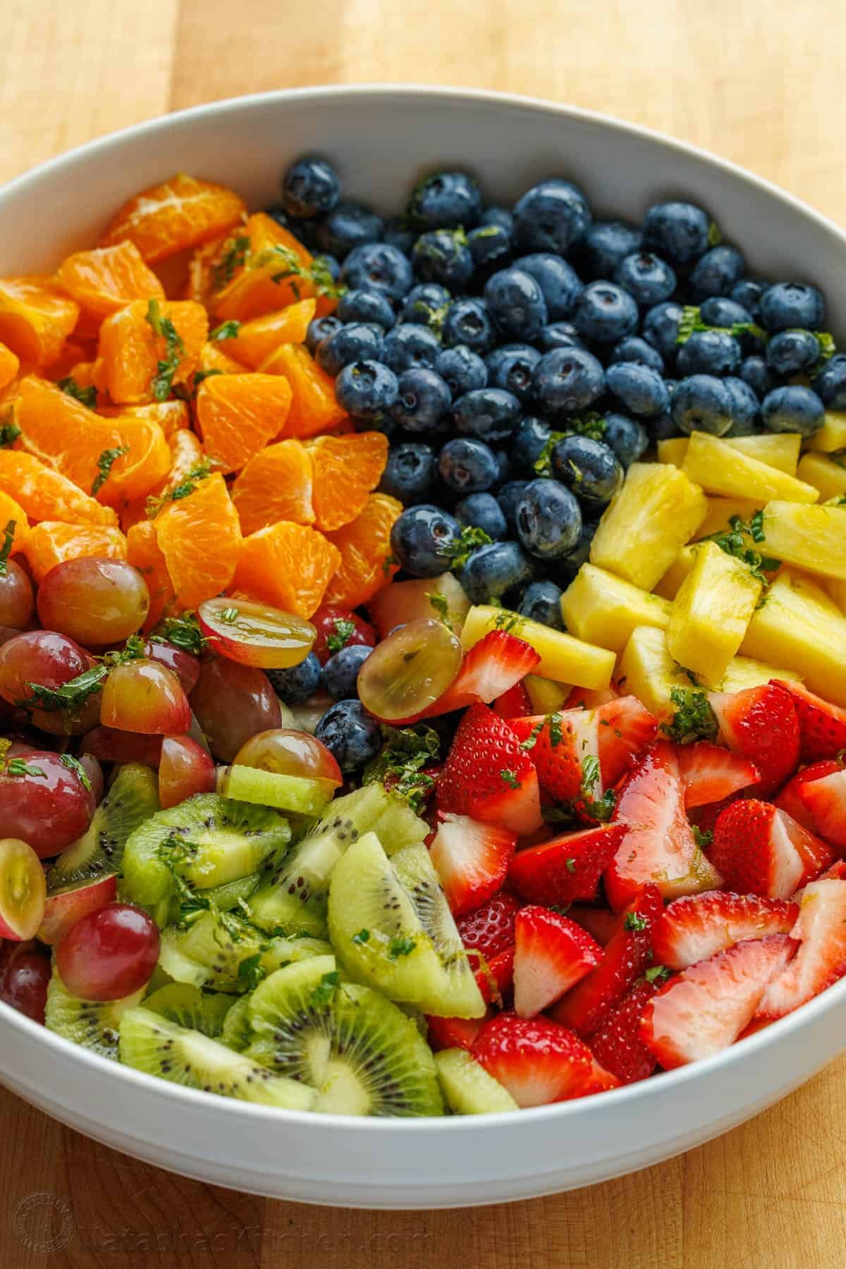 Classic Fruit Salad recipe features mixed fruit and a tasty honey-lime dressing. Bring this to your next potluck or gathering. Easy and fun! white serving bowl with mandarin oranges, blueberries, pineapple, strawberries, kiwi, and grapes.