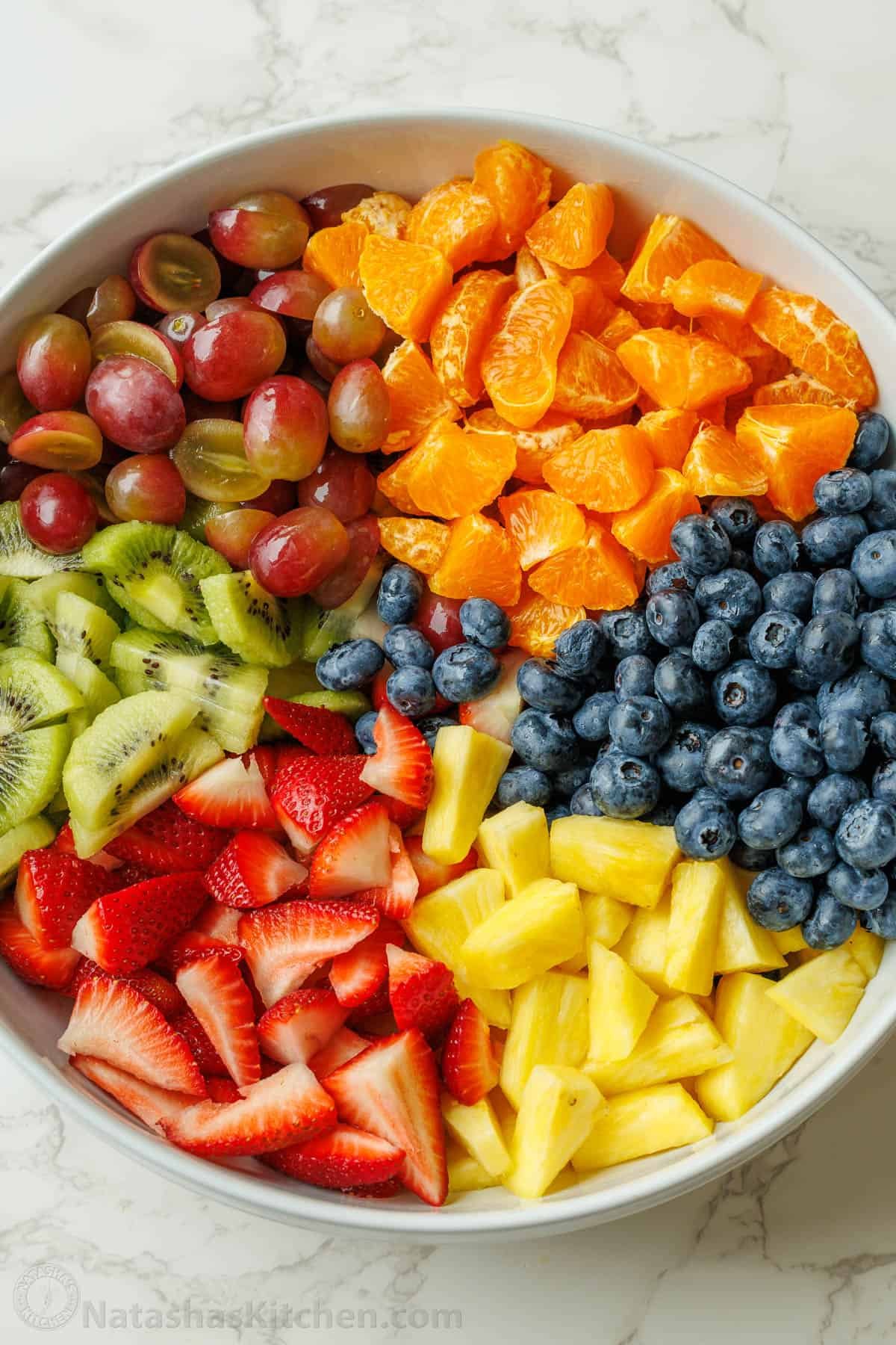 Classic Fruit Salad recipe features mixed fruit and a tasty honey-lime dressing. Bring this to your next potluck or gathering. Easy and fun! Large fruit salad recipe in a large white bowl with cut fruit