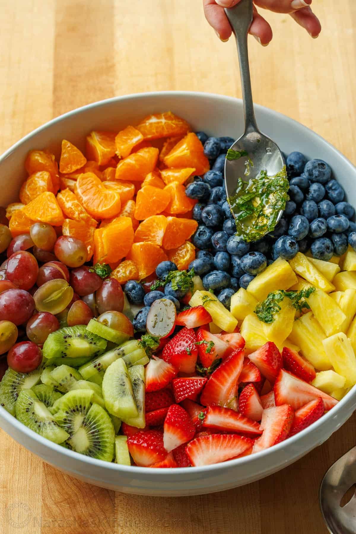 Classic Fruit Salad recipe features mixed fruit and a tasty honey-lime dressing. Bring this to your next potluck or gathering. Easy and fun! honey lime fruit salad dressing spooned onto cut fruit using a spoon
