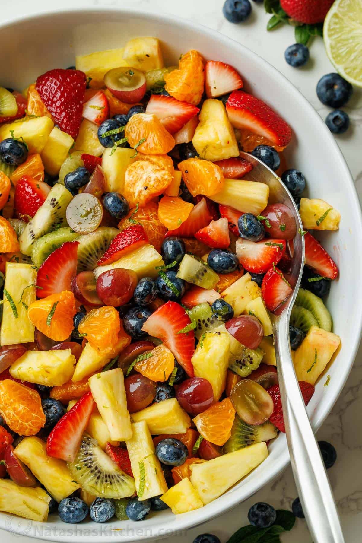Classic Fruit Salad recipe features mixed fruit and a tasty honey-lime dressing. Bring this to your next potluck or gathering. Easy and fun! Best of the fruit salad recipes in a large white bowl with serving spoon