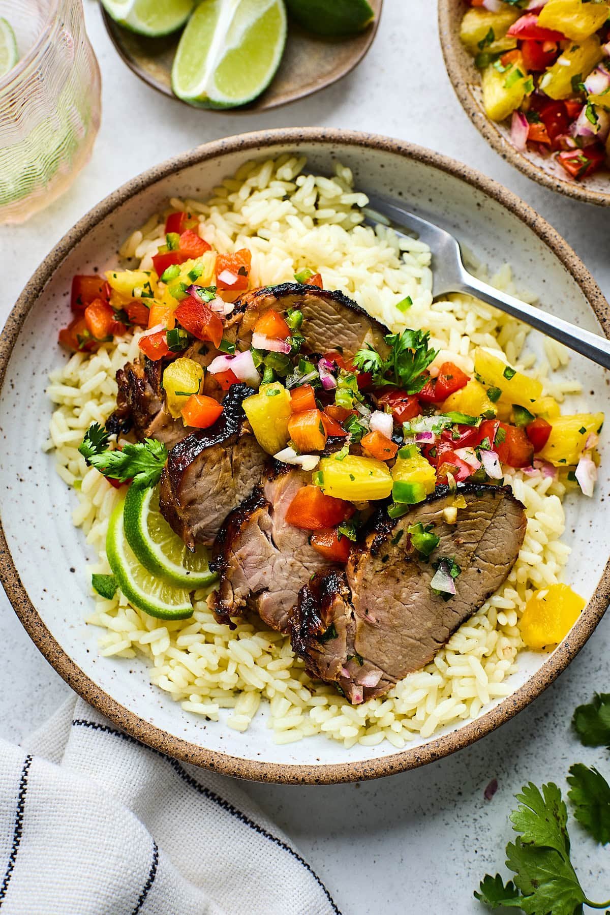 grilled pork tenderloin with pineapple salsa on plate with rice and fork. 