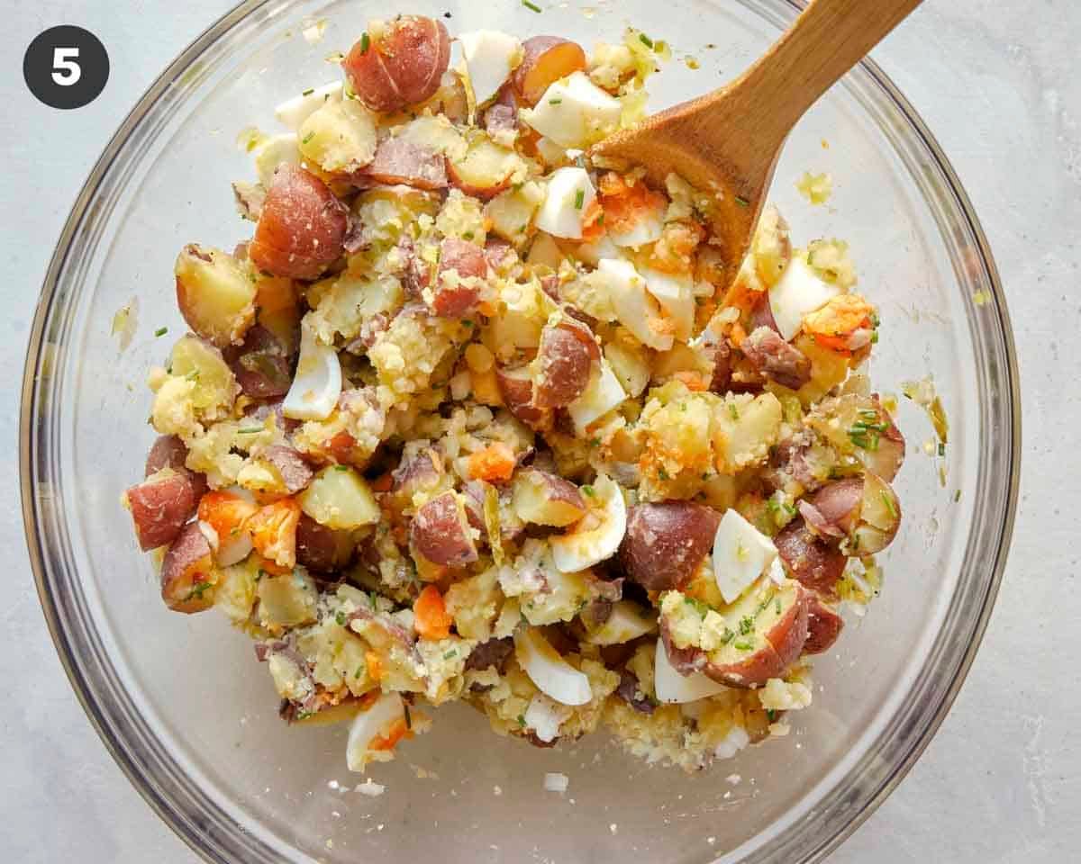 Potato salad with hard boiled eggs and potatoes being mixed in a bowl.