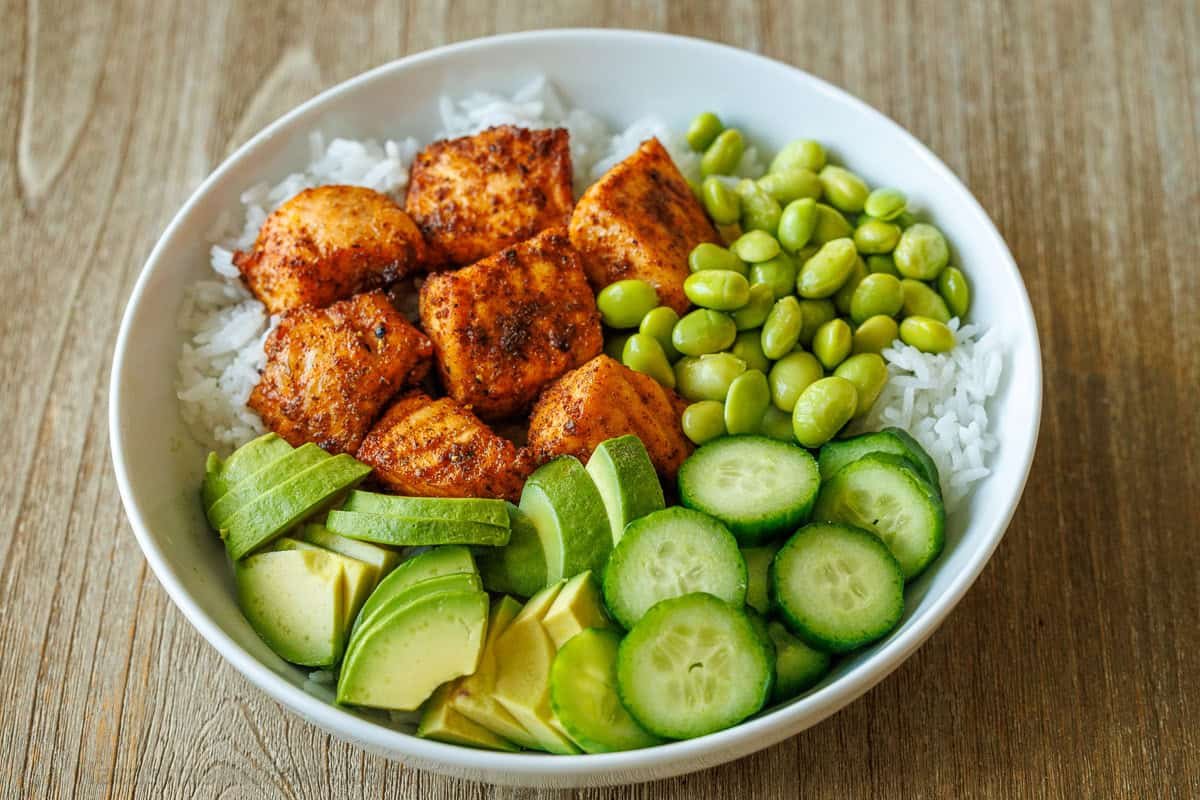 Easy salmon bowl recipe with air fryer salmon chunks, edamame, cucumbers, rice and avocado in a white bowl