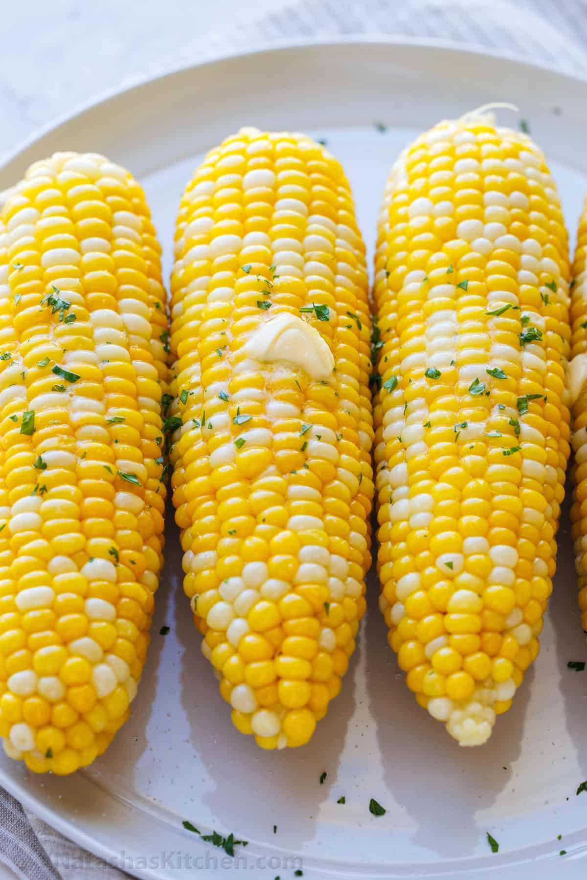 hot boiled corn on the cob on a serving tray topped with butter and parsley
