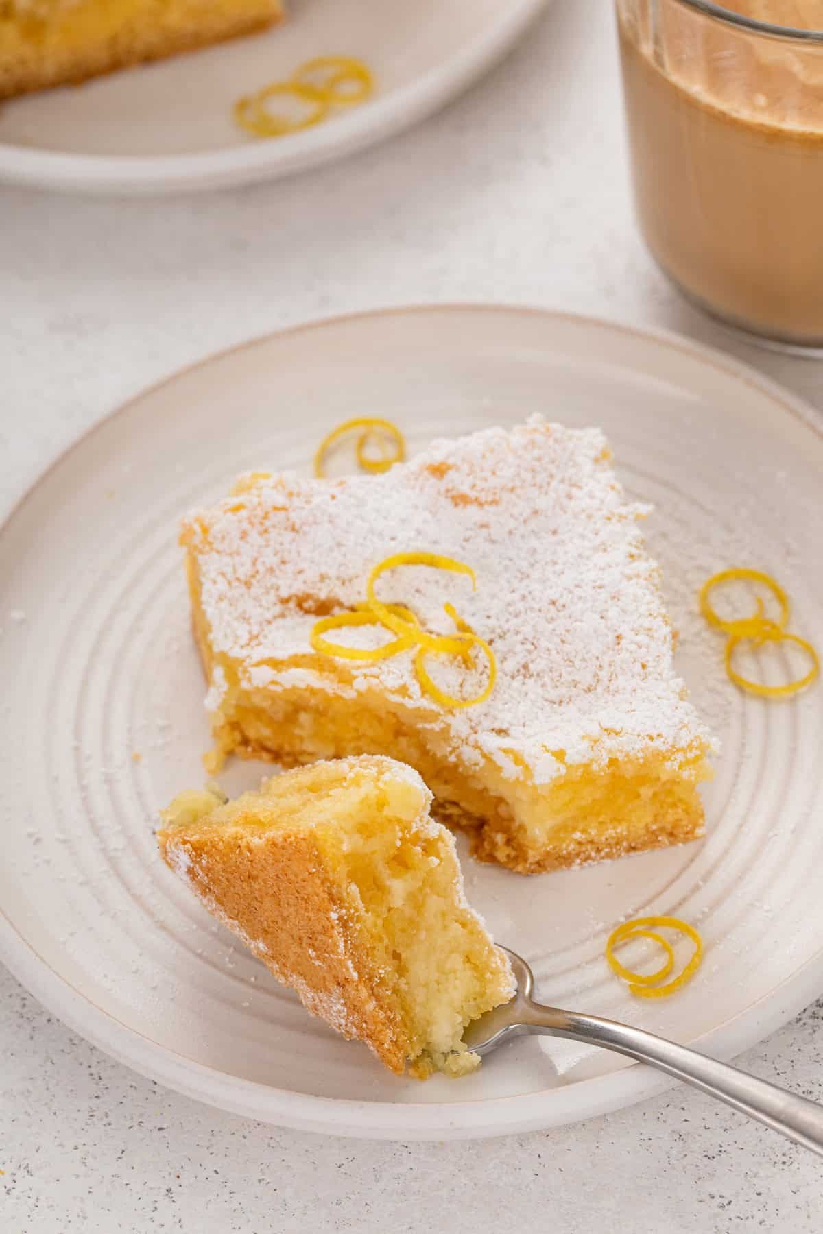 Fork cutting a bite from the corner of a slice of lemon gooey butter cake.