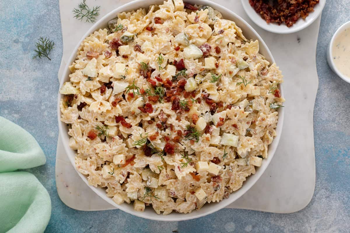 Overhead view of a large serving bowl filled with dill pickle pasta salad, topped with crumbled bacon.