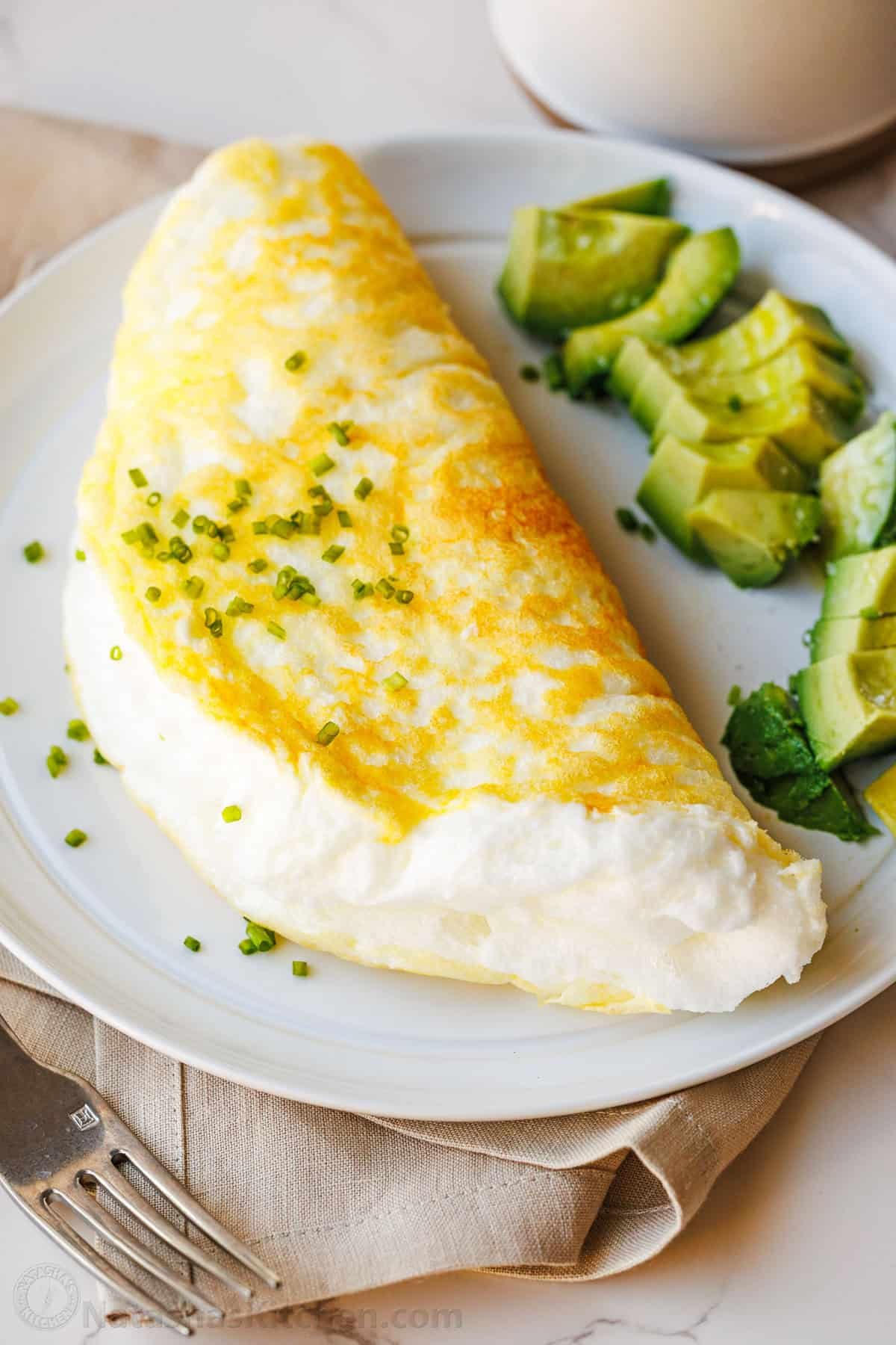 Make a fluffy egg white omelette in just 10 minutes with 4 ingredients. It’s light, airy, high-protein, and easy to customize with toppings. soufflé omelette with egg whites on a plate with sliced avocado and a beige napkin