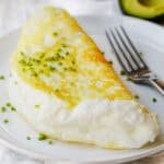 Souffle style fluffy egg white omelette folded on a plate with chives to garnish and fork to eat.