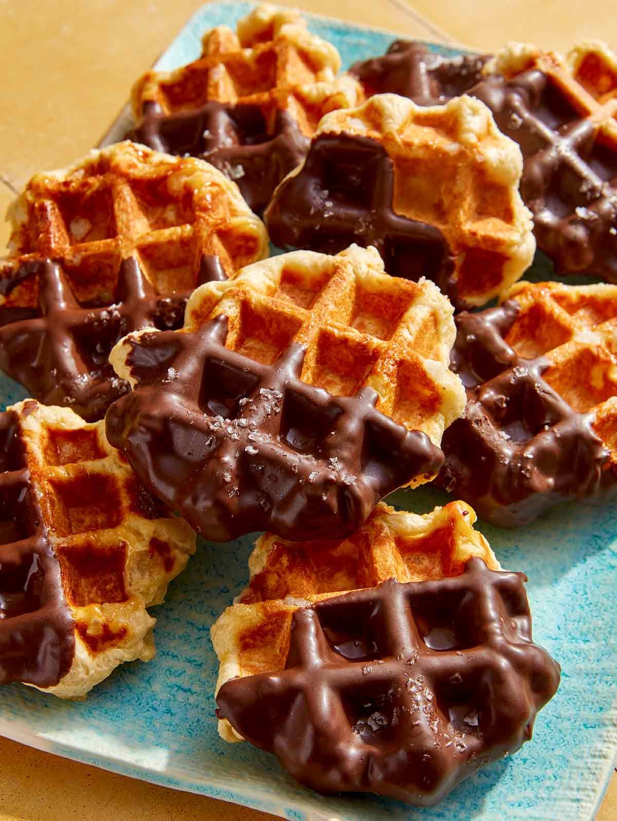 Liege waffles dipping in chocolate on a platter.