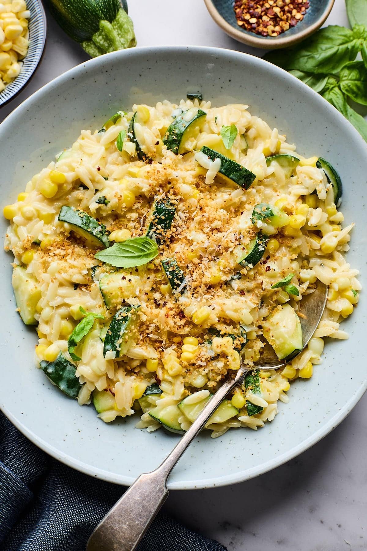 corn and zucchini orzo with toasted garlic breadcrumbs in bowl with fresh basil and spoon. 