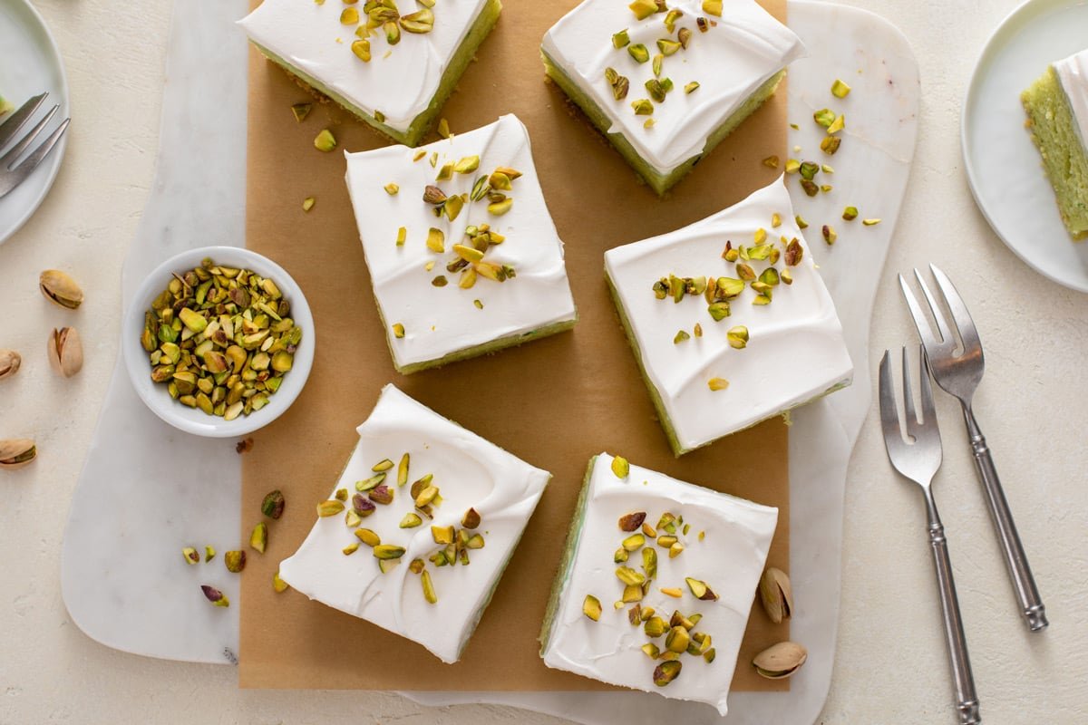 Overhead view of slices of pistachio poke cake garnished with chopped pistachios arranged on a wooden board.