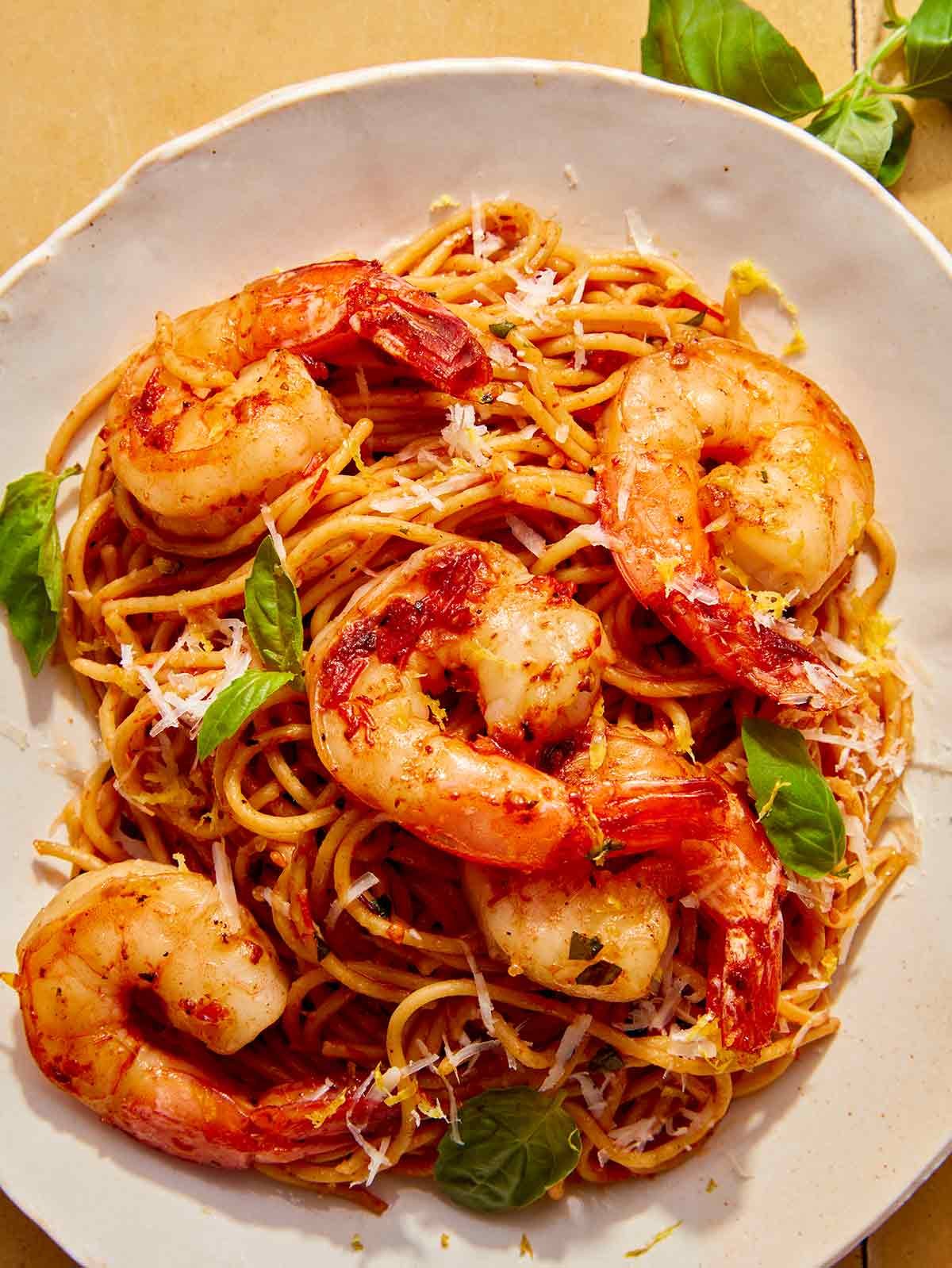 Shrimp pasta with tomato butter sauce and fresh basil on a white plate.