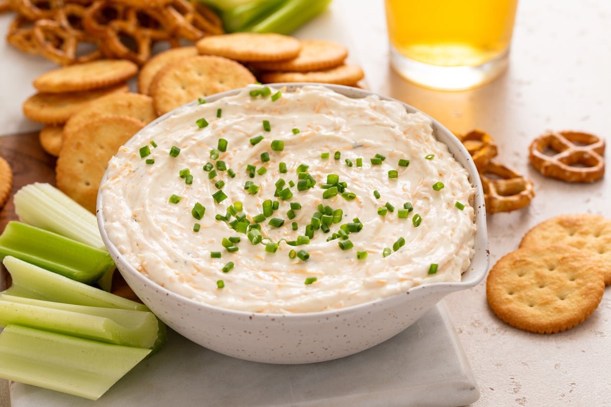 White bowl filled with ranch beer cheese dip surrounded by crackers, celery, and pretzel twists.