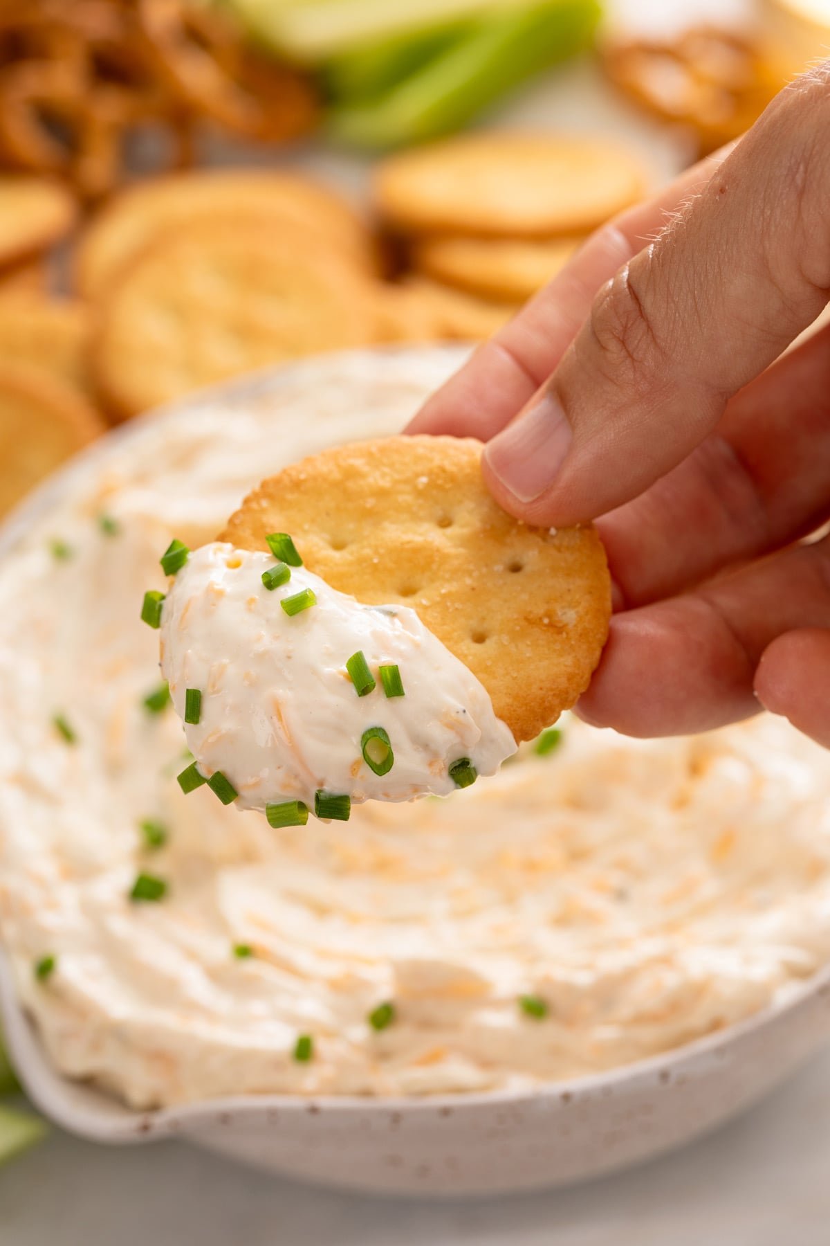 Hand holding a cracker with ranch beer cheese dip on it.