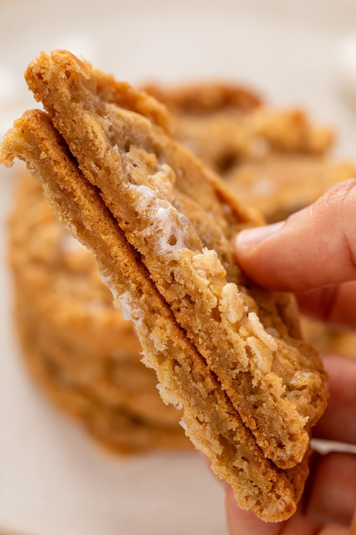 Hand holding a rice krispie cookie that has been cut in half to show the chewy texture inside of the cookie.