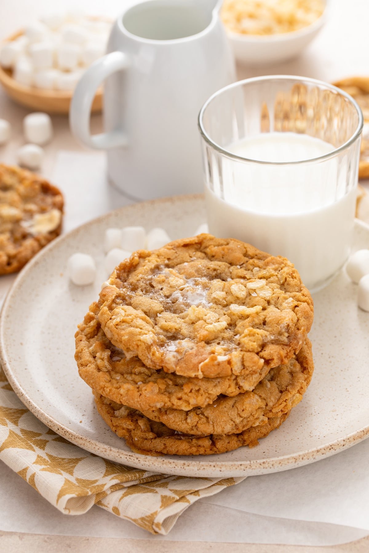 4 rice krispie cookies stacked on a white plate next to a glass of milk.