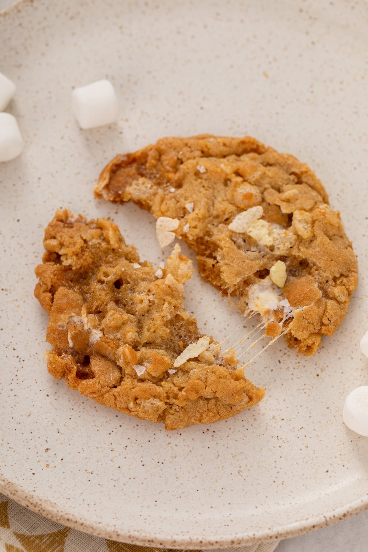 Rice krispie cookie that has been broken in half on a plate to show the gooey marshmallow.