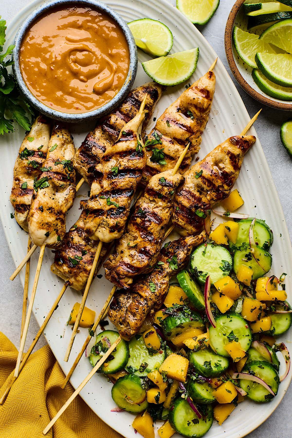 chicken satay skewers on platter with peanut sauce and cucumber mango salad.