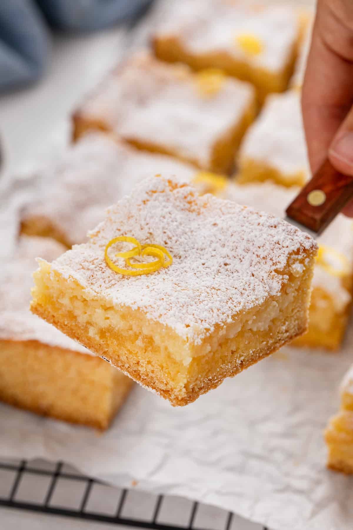 Cake server lifting up a slice of lemon gooey butter cake dusted with powdered sugar.