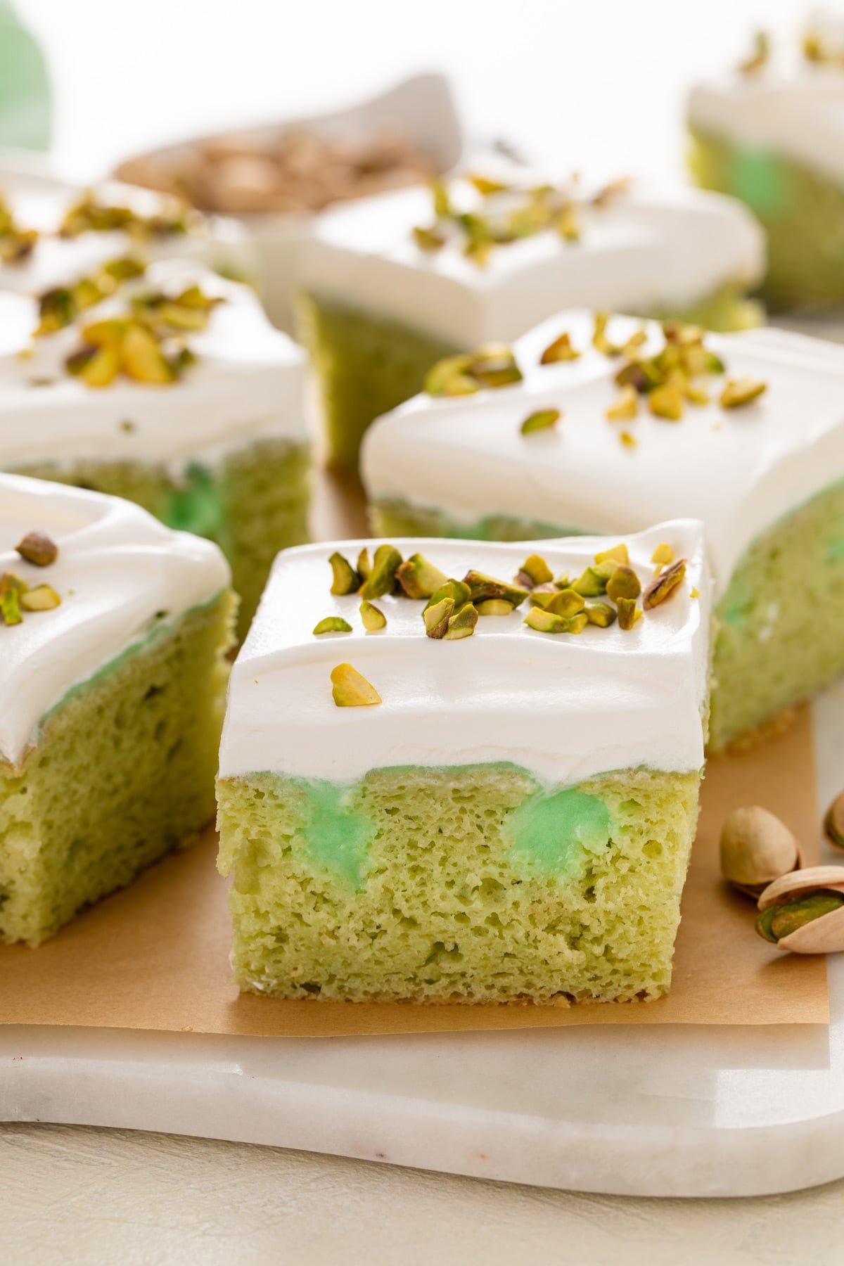 Close up of the side view of a slice of pistachio poke cake to show pistachio pudding in the holes of the cake.