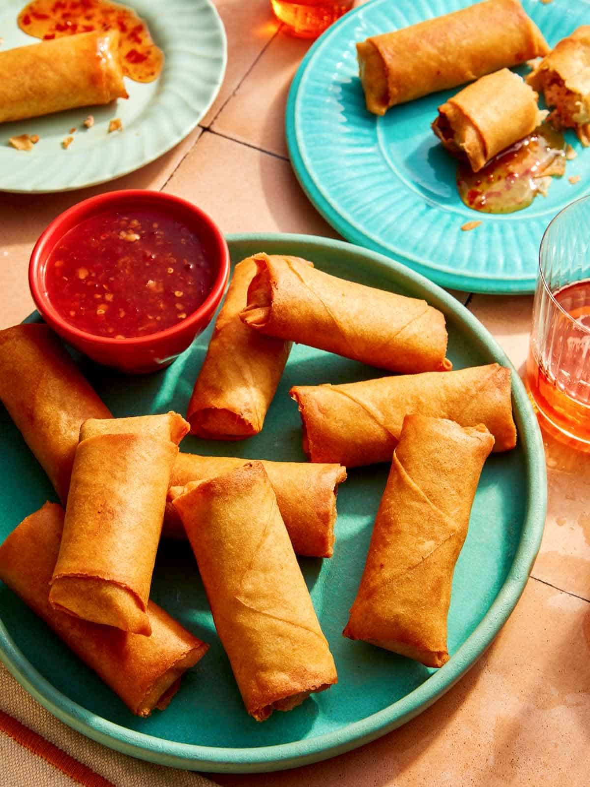 A platter of spring rolls with some being served on plates in the background.