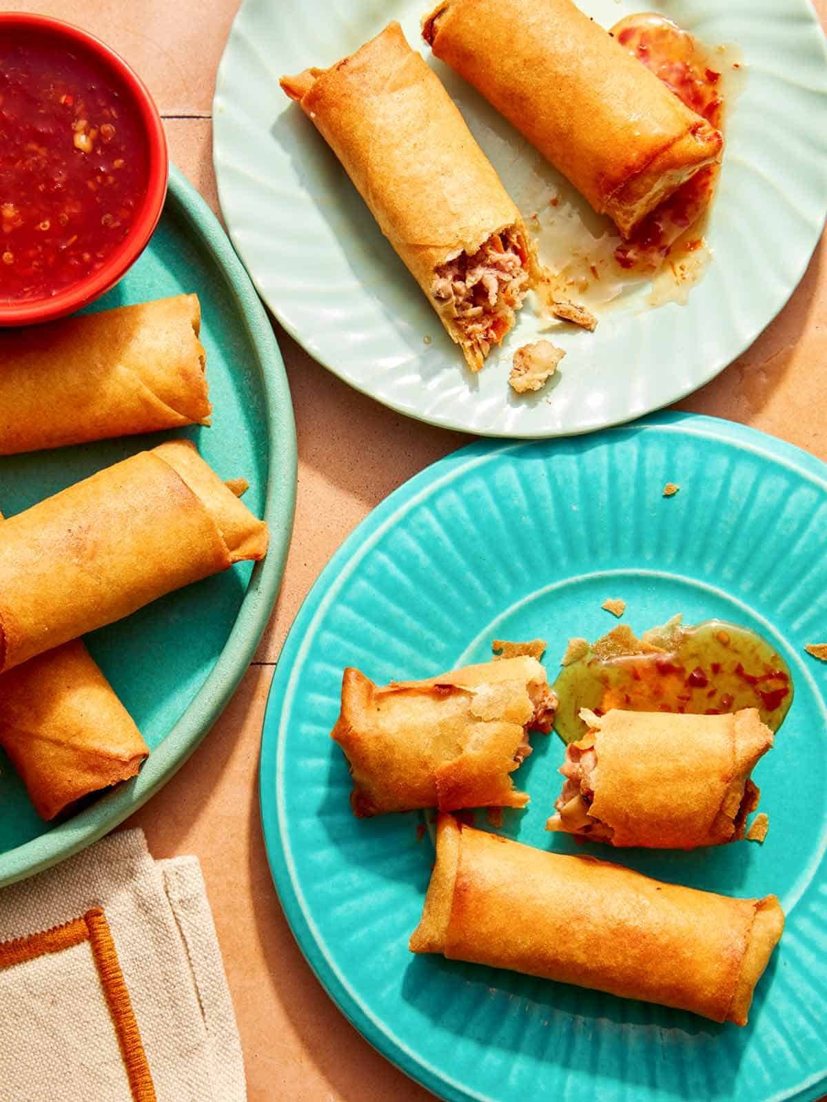Three plates of partially eaten spring rolls and sauce.