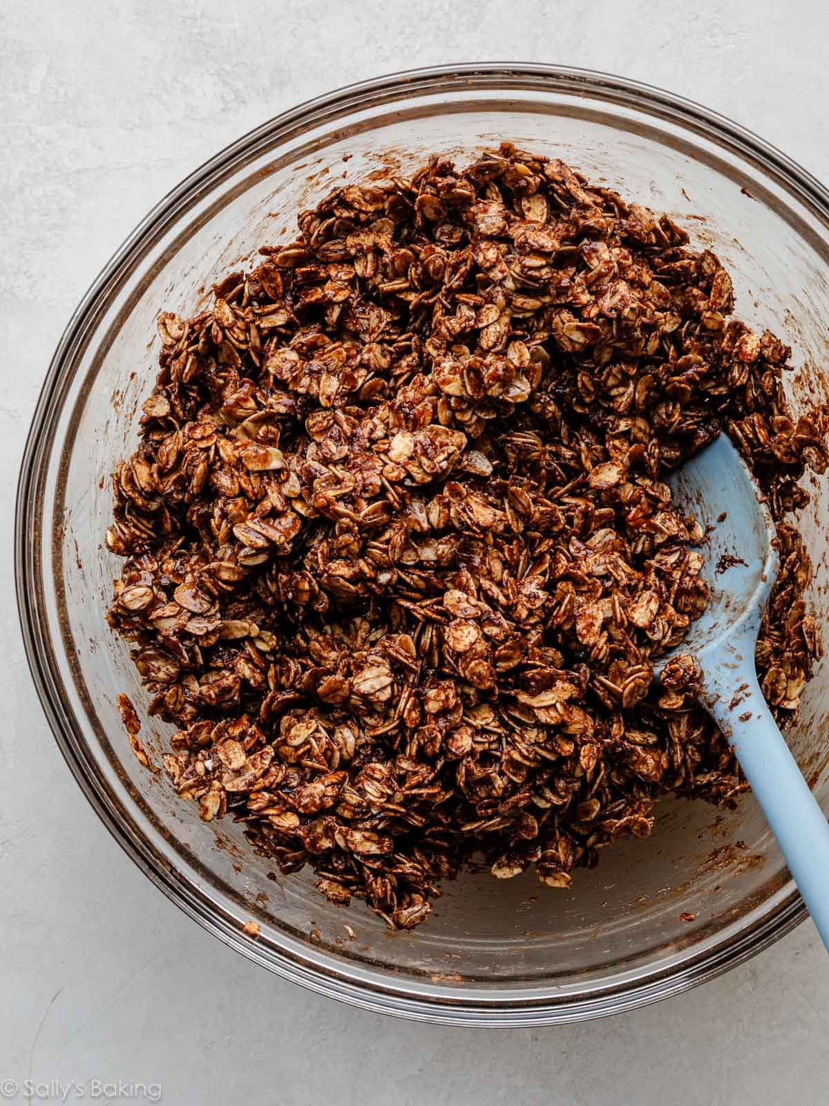 spatula stirring chocolate crunch granola mixture in a glass bowl.
