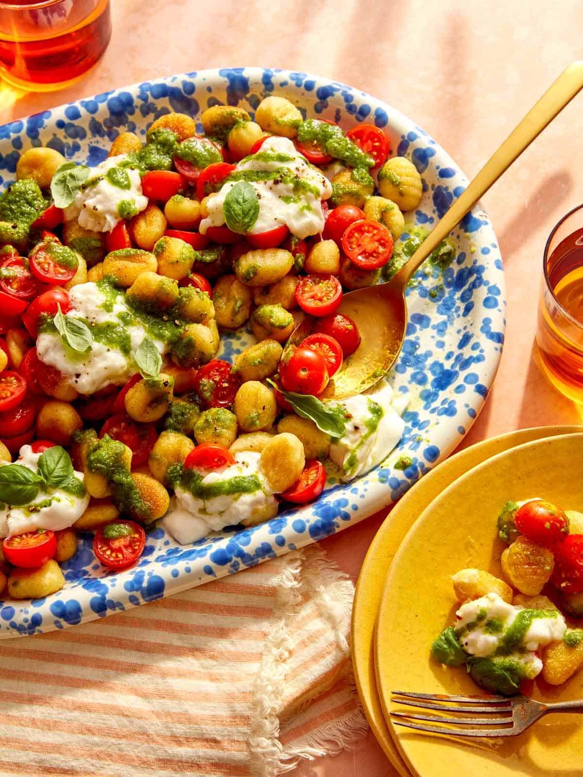 Caprese gnocchi that was pan fried on a platter with some being served onto plates.