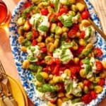 Caprese gnocchi on a platter with some plates on the side.