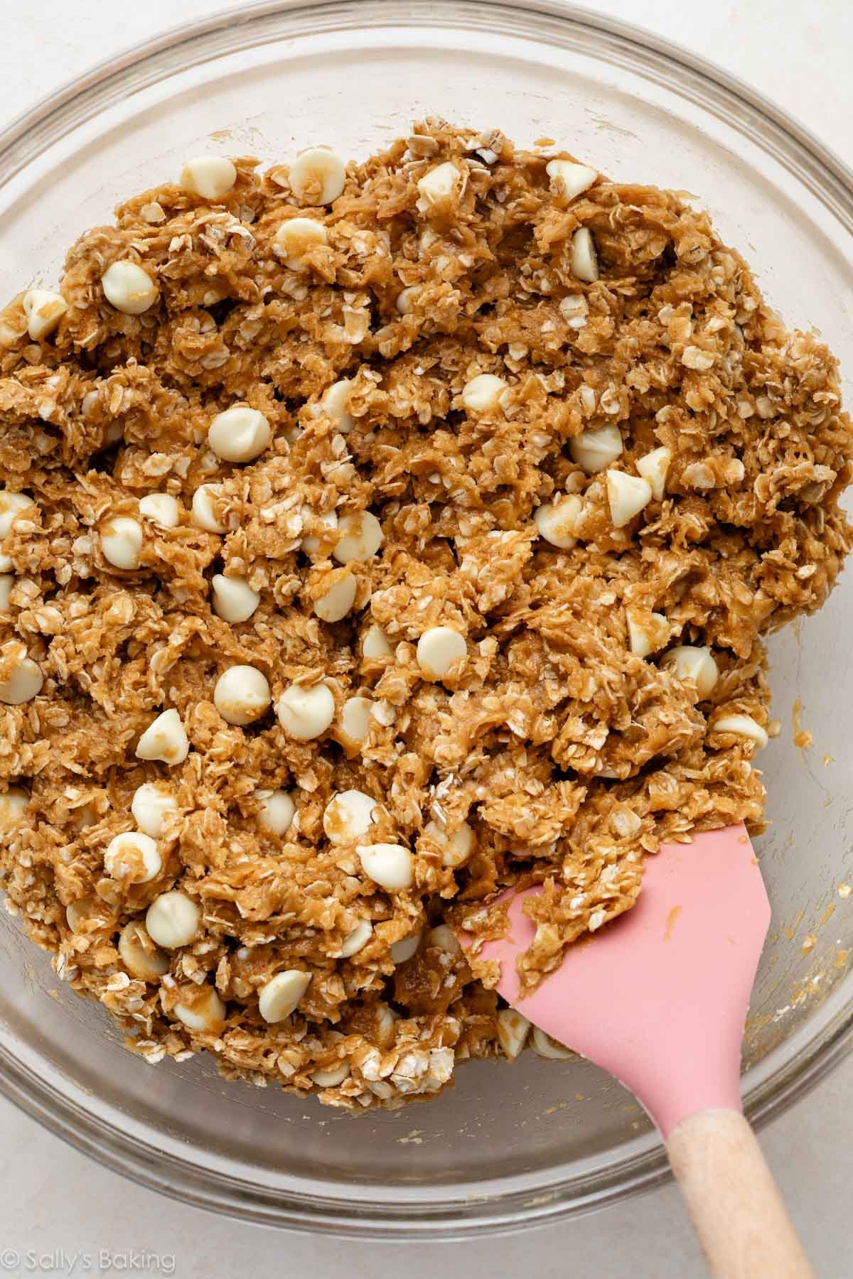 Pink spatula stirring Biscoff white chocolate oatmeal cookie dough in a glass bowl.