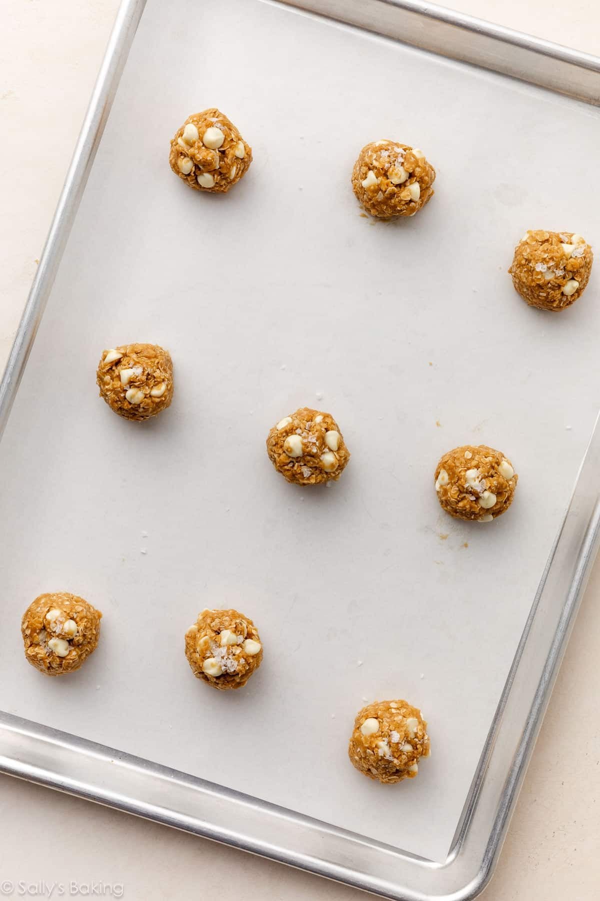 9 cookie dough balls on a lined baking sheet topped with sea salt flakes.