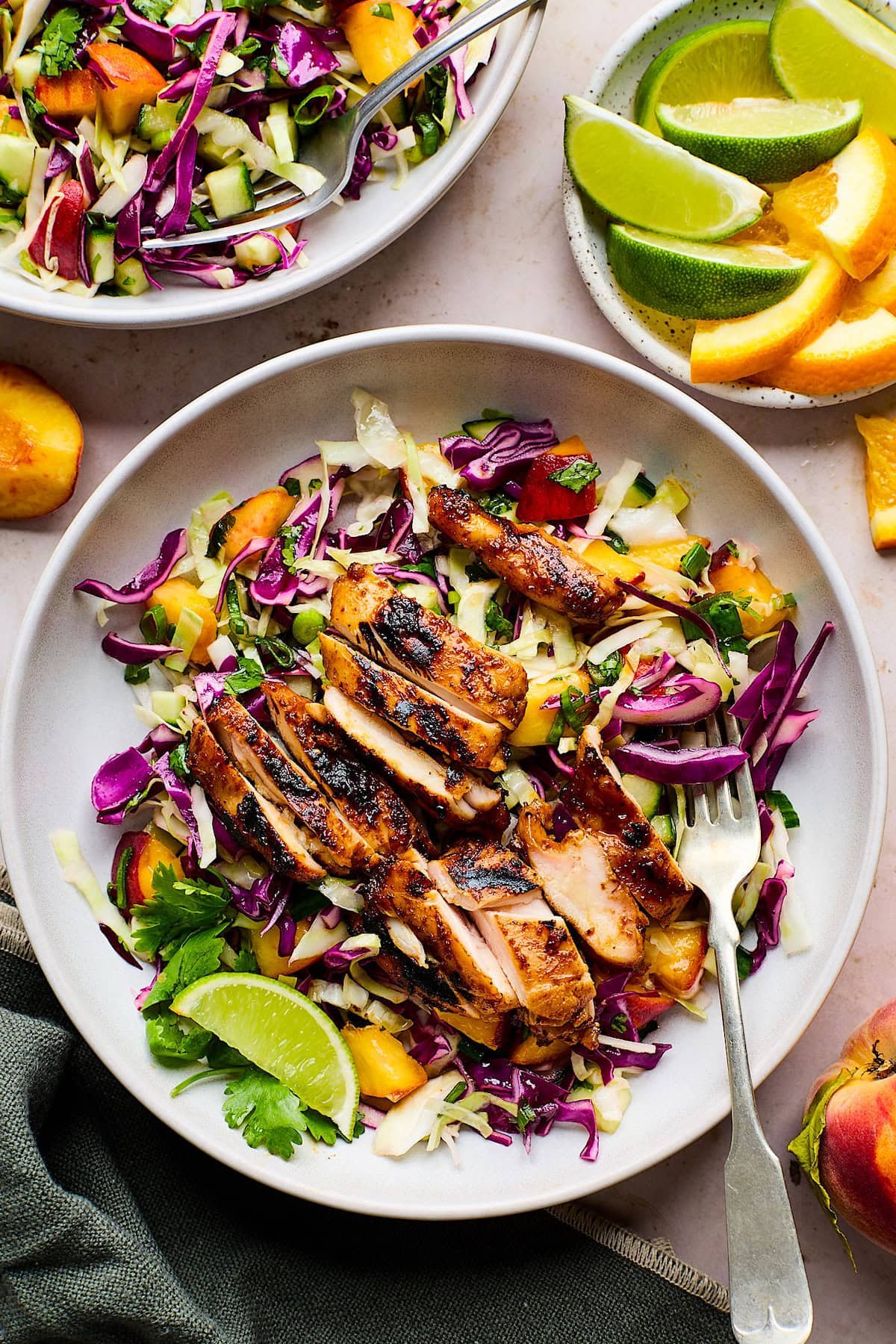 honey chipotle chicken thighs sliced over peach slaw in bowl with fork. 