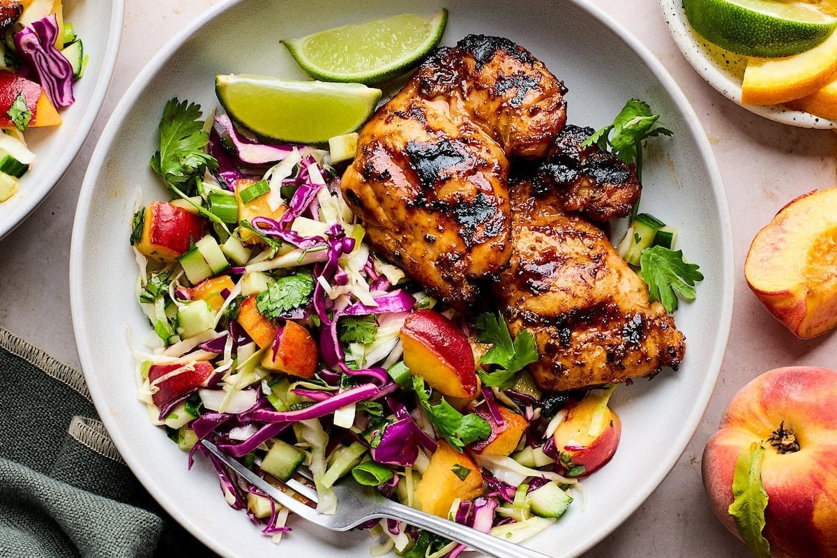 honey chipotle chicken thighs with peach slaw on plate with lime wedges. 