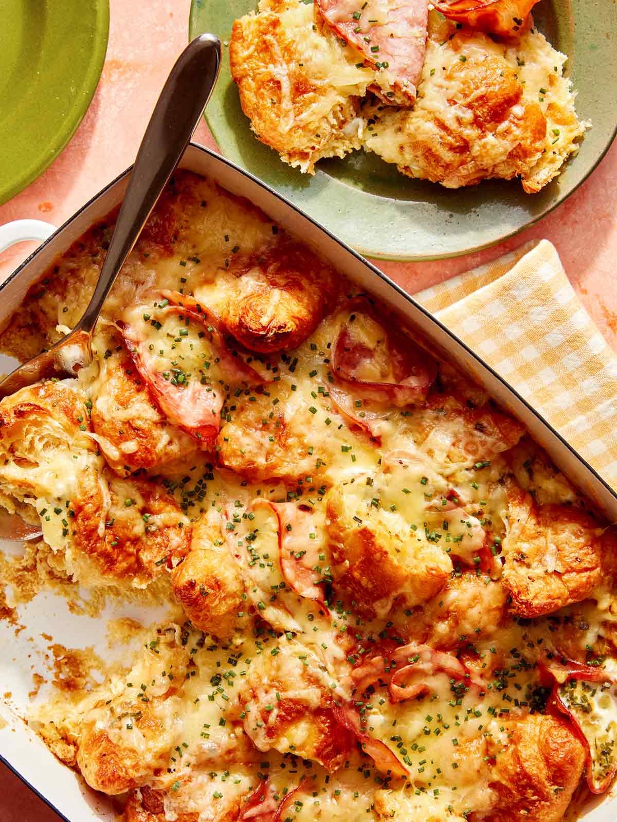 Close up on a ham and cheese croissant bake with some served on a plate.