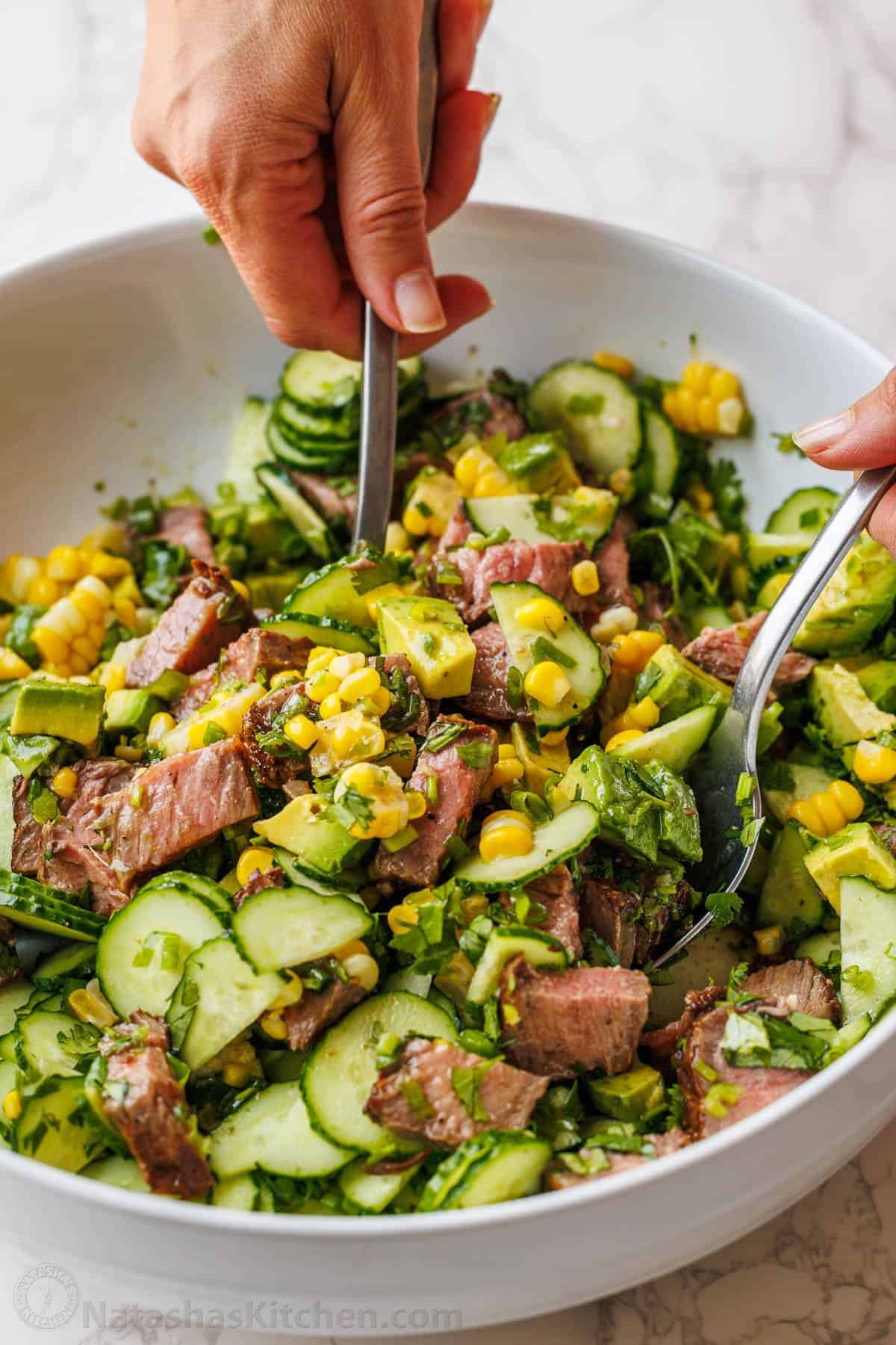 Steak Salad recipe with pan-seared steak, cucumber, corn, avocado, cilantro, and jalapeño, tossed with a vibrant honey-lime dressing. mixing steak salad in a bowl with corn, cucumber, cilantro, and avocado