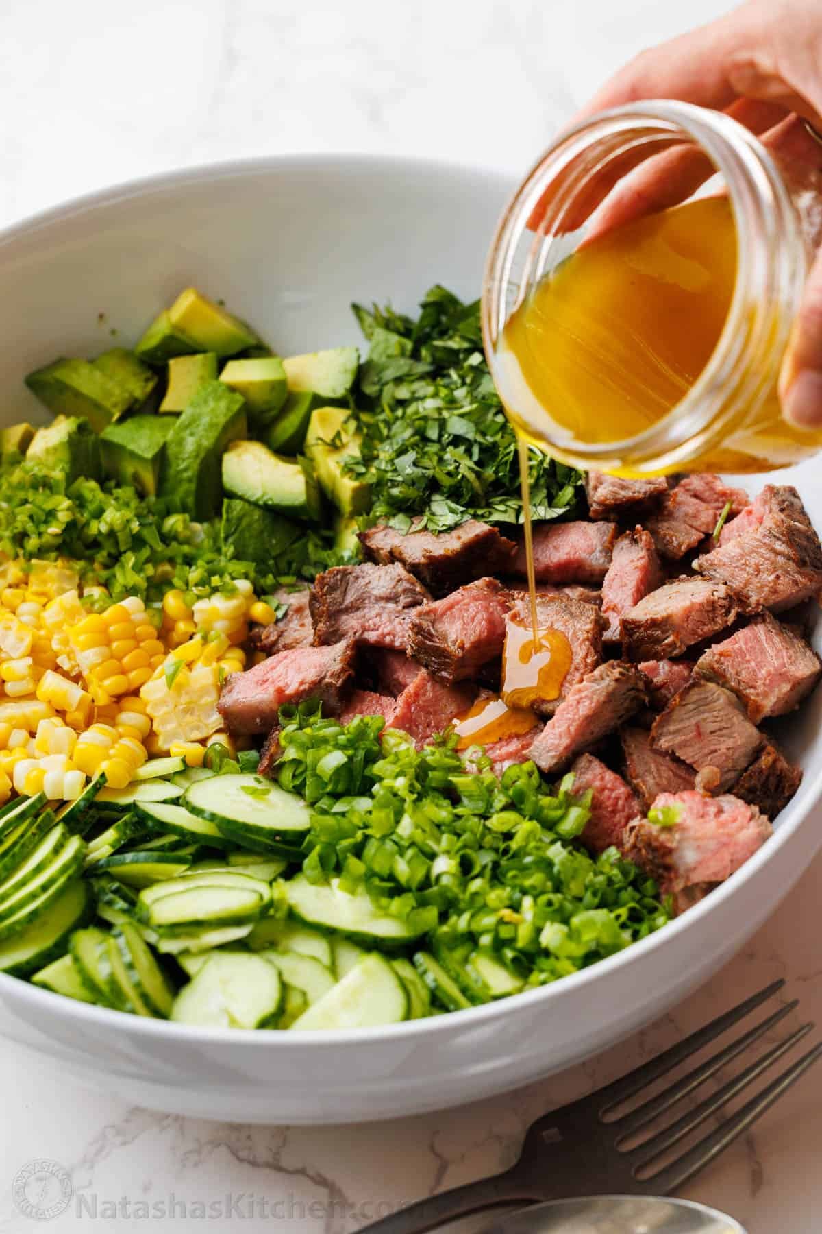 Steak Salad recipe with pan-seared steak, cucumber, corn, avocado, cilantro, and jalapeño, tossed with a vibrant honey-lime dressing. Pouring dressing from a mason jar over high-protein dinner recipe