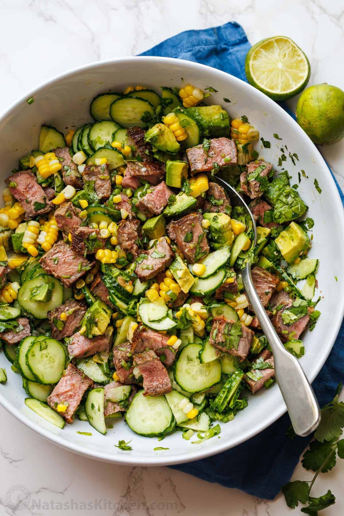 Steak Salad recipe with pan-seared steak, cucumber, corn, avocado, cilantro, and jalapeño, tossed with a vibrant honey-lime dressing. Steak Salad mixed in a bowl with corn, cucumbers, avocado and honey lime dressing