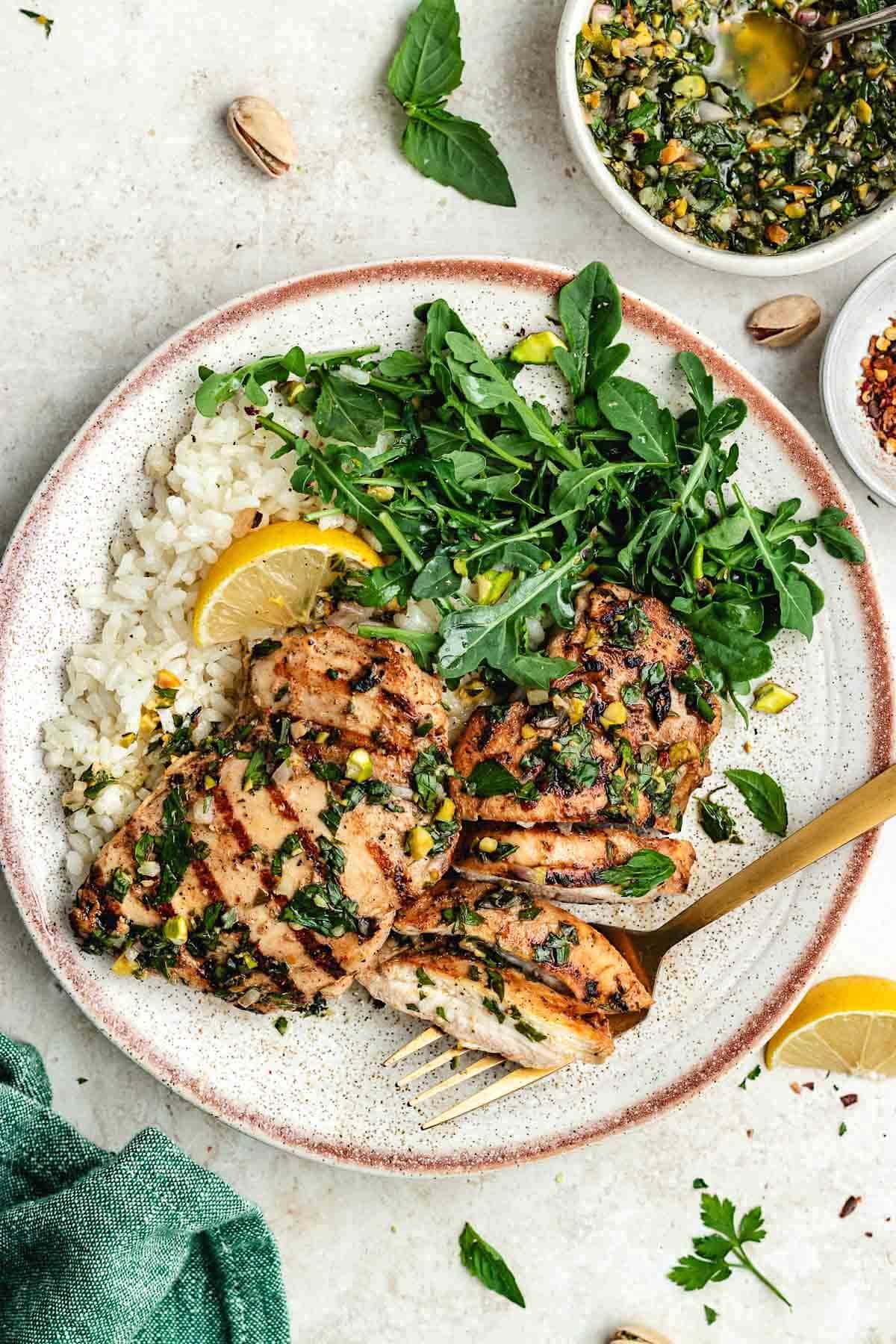 grilled lemon herb chicken thighs on plate with rice and salad. 
