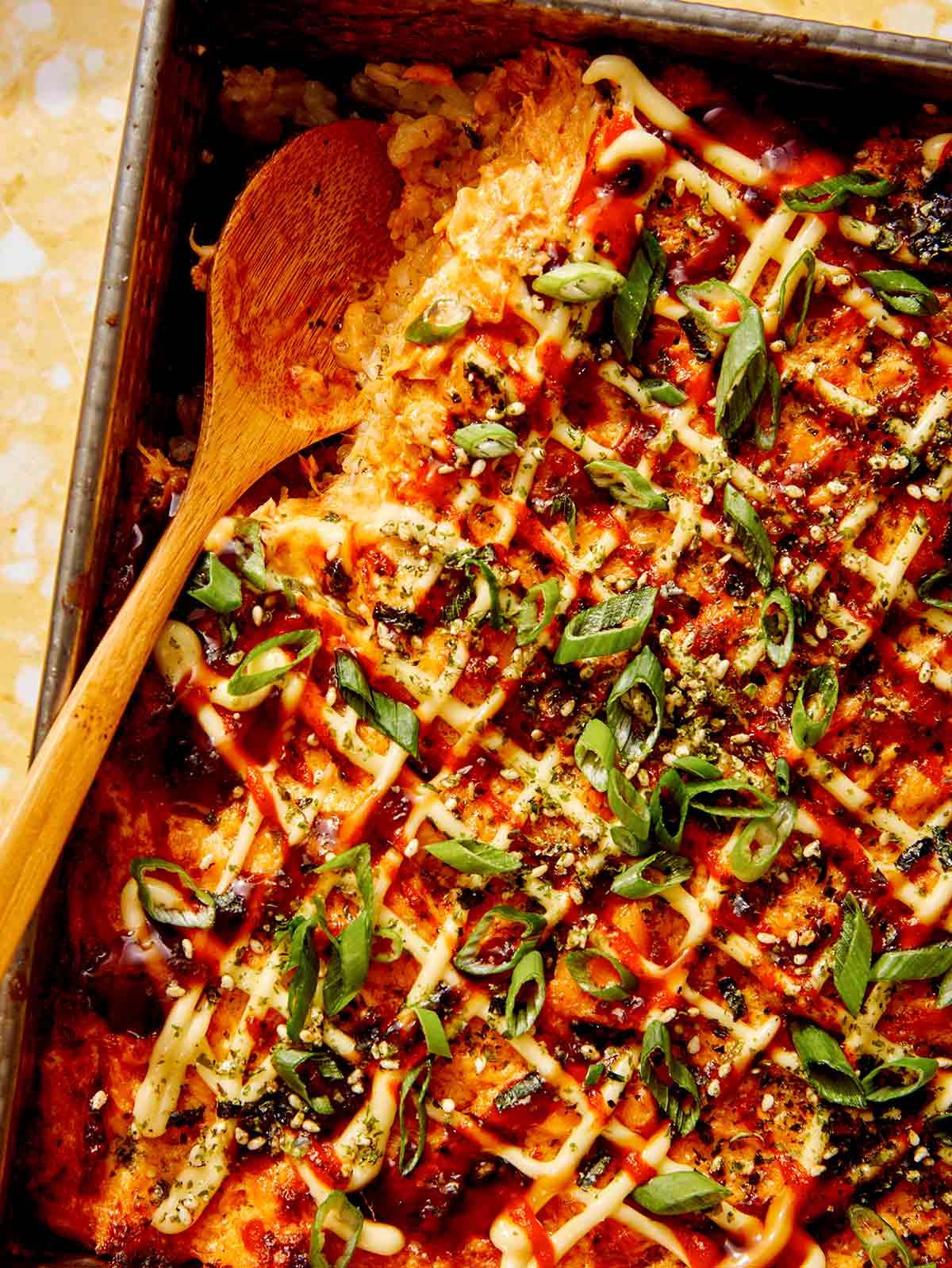 Close up on a baking dish of sushi bake recipe with a spoon in it.