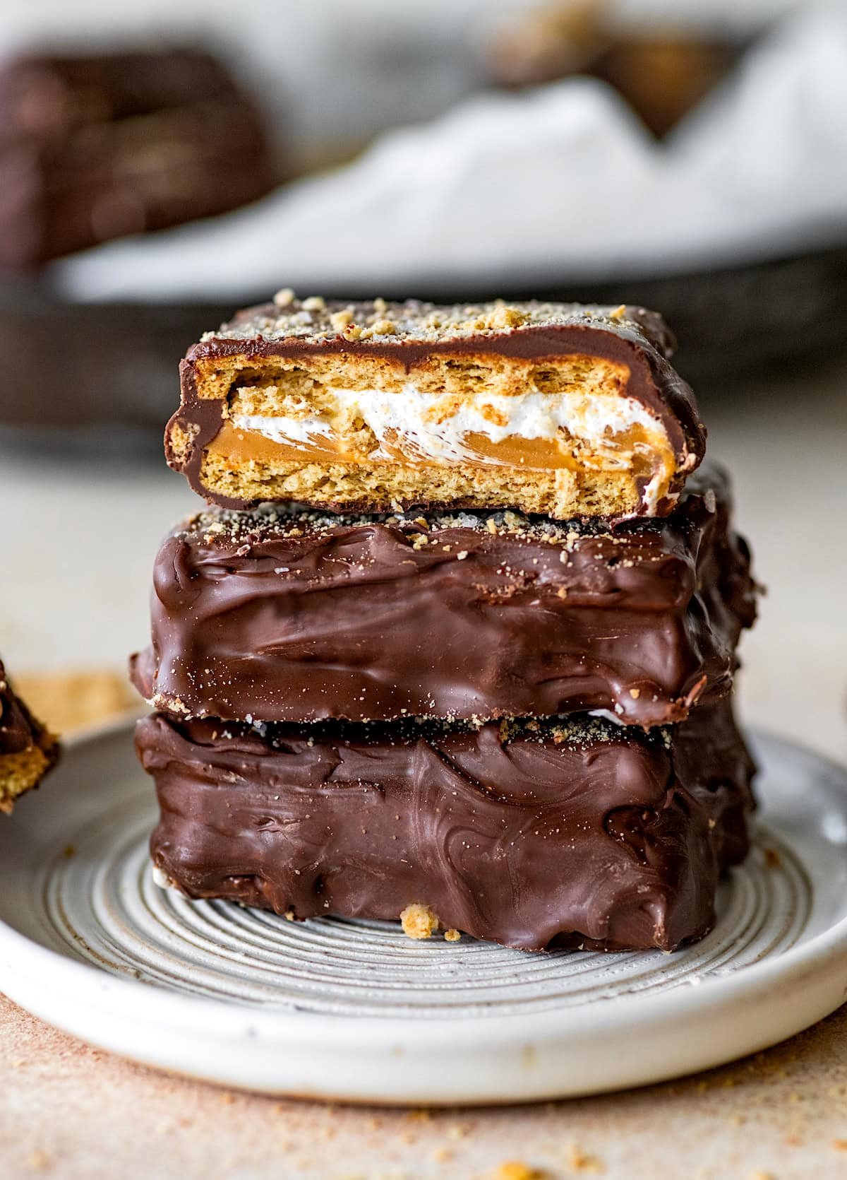 chocolate covered s'mores graham cracker sandwiches with peanut butter stacked on a plate.