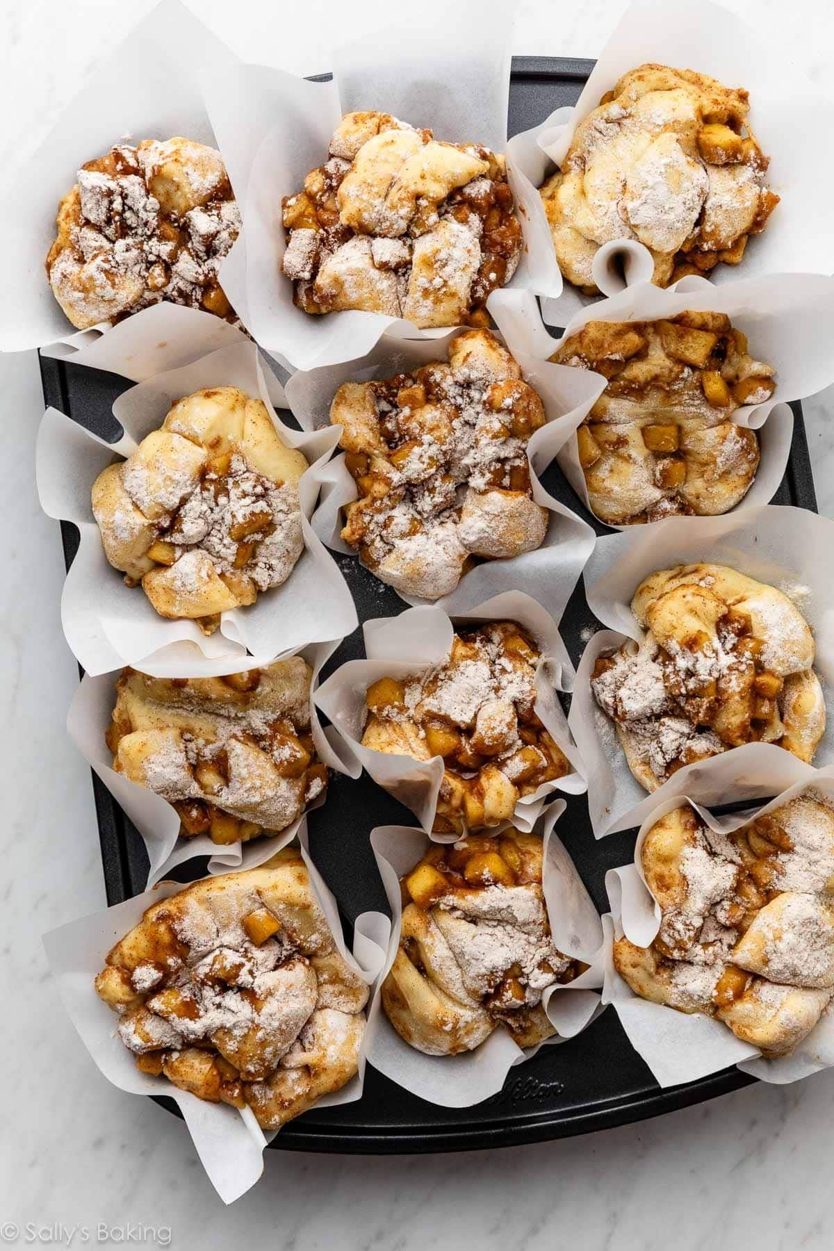 uncooked apple fritters in parchment paper lined muffin pan.