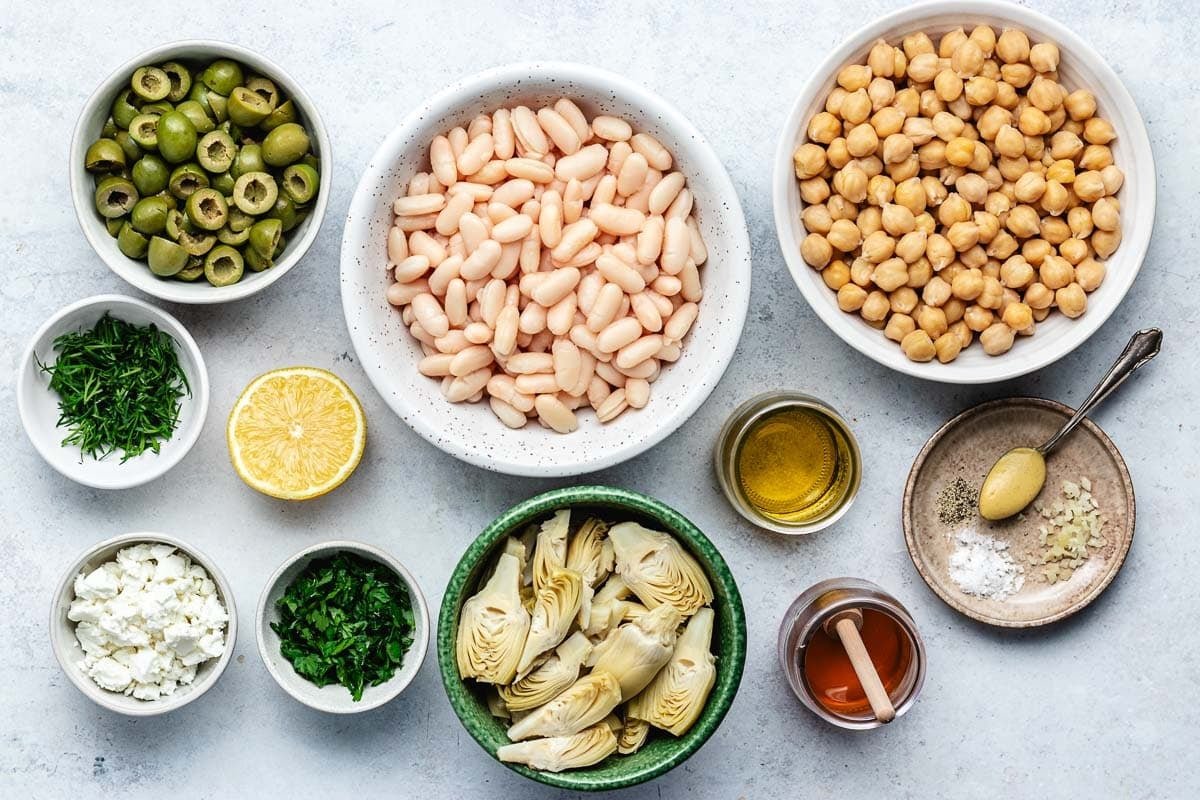 ingredients in bowls to make bean salad with artichokes, olives, and feta. 